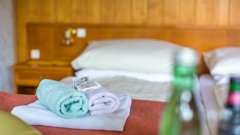 Hotelzimmer mit Bett, Handtüchern und Wasserflaschen.