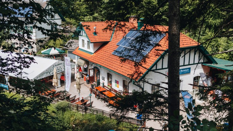 Ein traditionelles Gasthaus mit Solarpanelen auf dem Dach, umgeben von Bäumen.