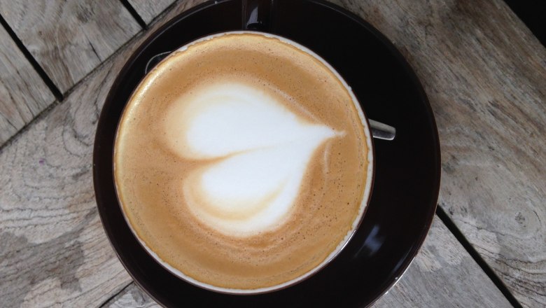 A cup of cappuccino with heart latte art on a wooden table.