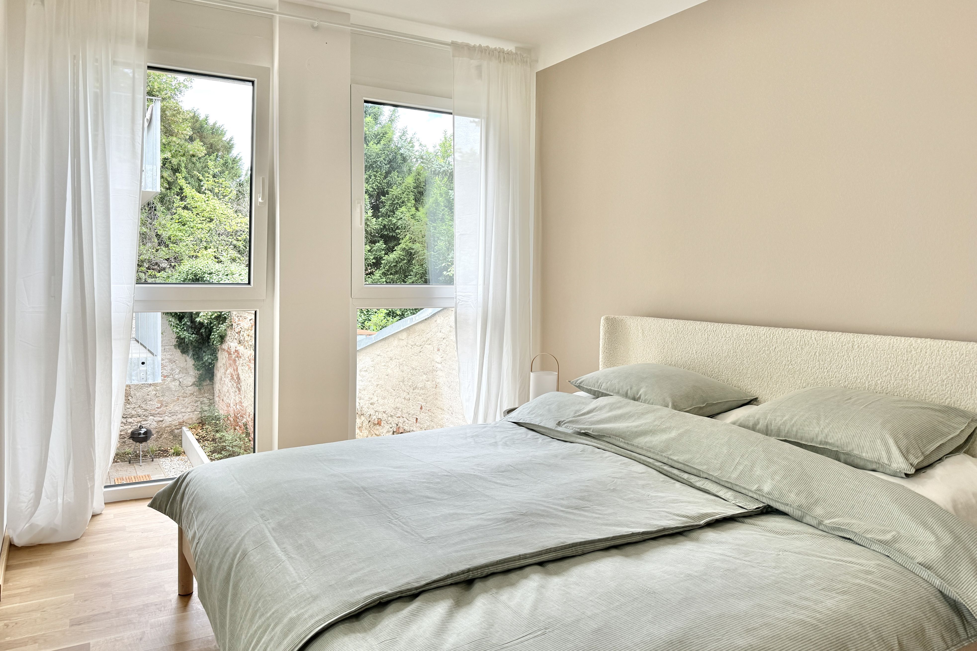 Beiges Schlafzimmer mit großen Fenstern und bequemen Bett