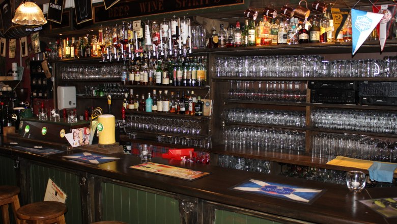 A bar with a large selection of whisky bottles and glasses on shelves.