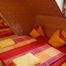 Gemütlicher Schlafraum mit Holzwänden und bunten Betten in einem Berggasthof.
