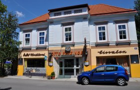 Außenansicht eines Cafés mit blauer Fassade und rotem Dach, davor ein blaues Auto geparkt.