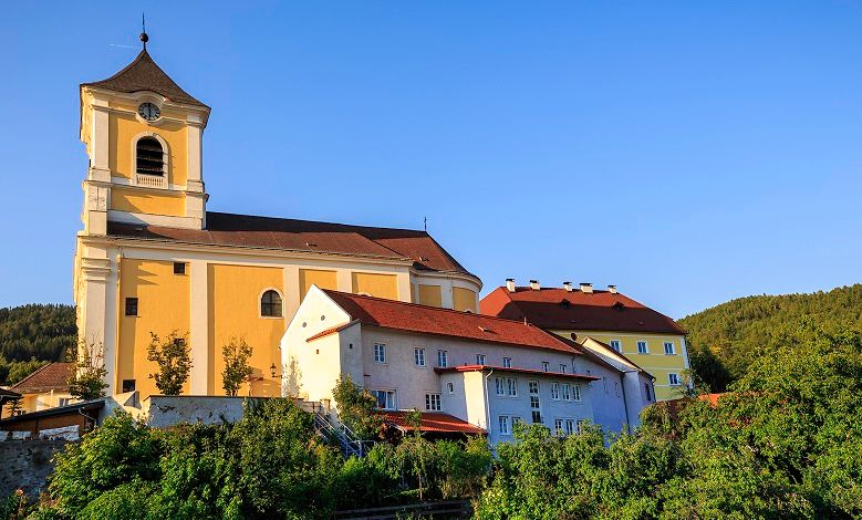 Kirche mit angrenzendem Kloster auf einem Hügel bei klarem Himmel.