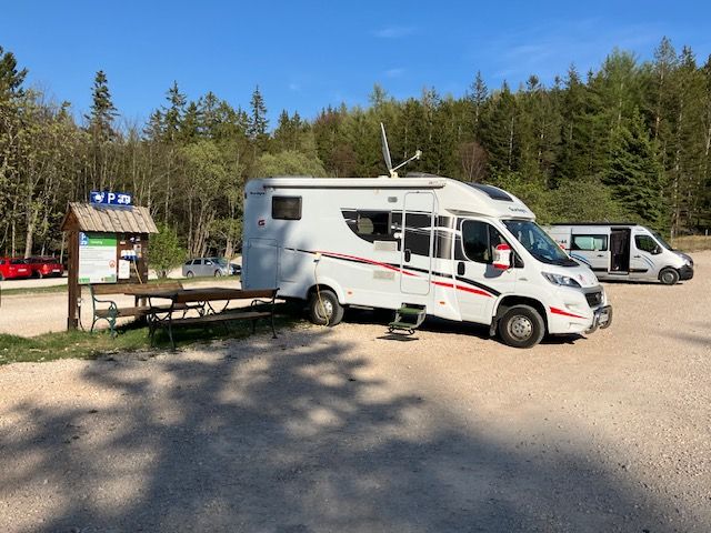 Wohnmobil auf einem Parkplatz im Naturpark Hohe Wand, umgeben von Bäumen und einem blauen Himmel.