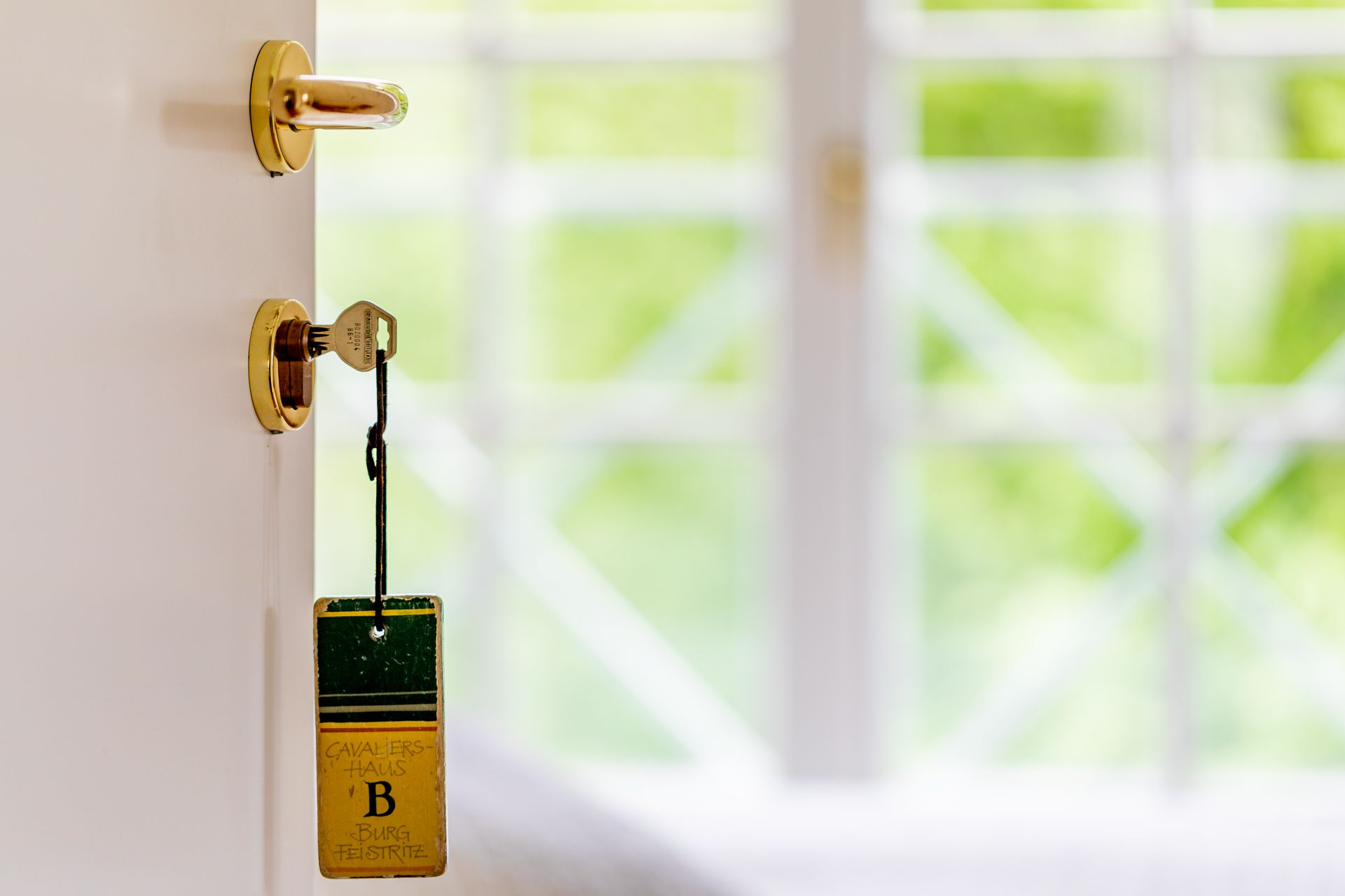 Ein Schlüssel steckt in einer Tür mit einem Anhänger, auf dem "Kavaliershaus B Burg Feistritz" steht.