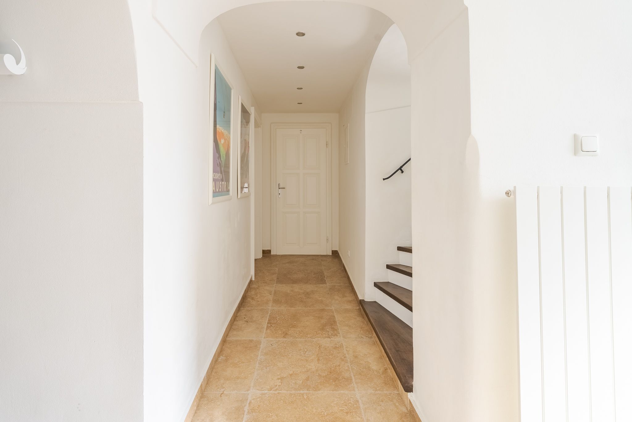 Ein heller Flur mit weißen Wänden, Fliesenboden und einer Treppe auf der rechten Seite.