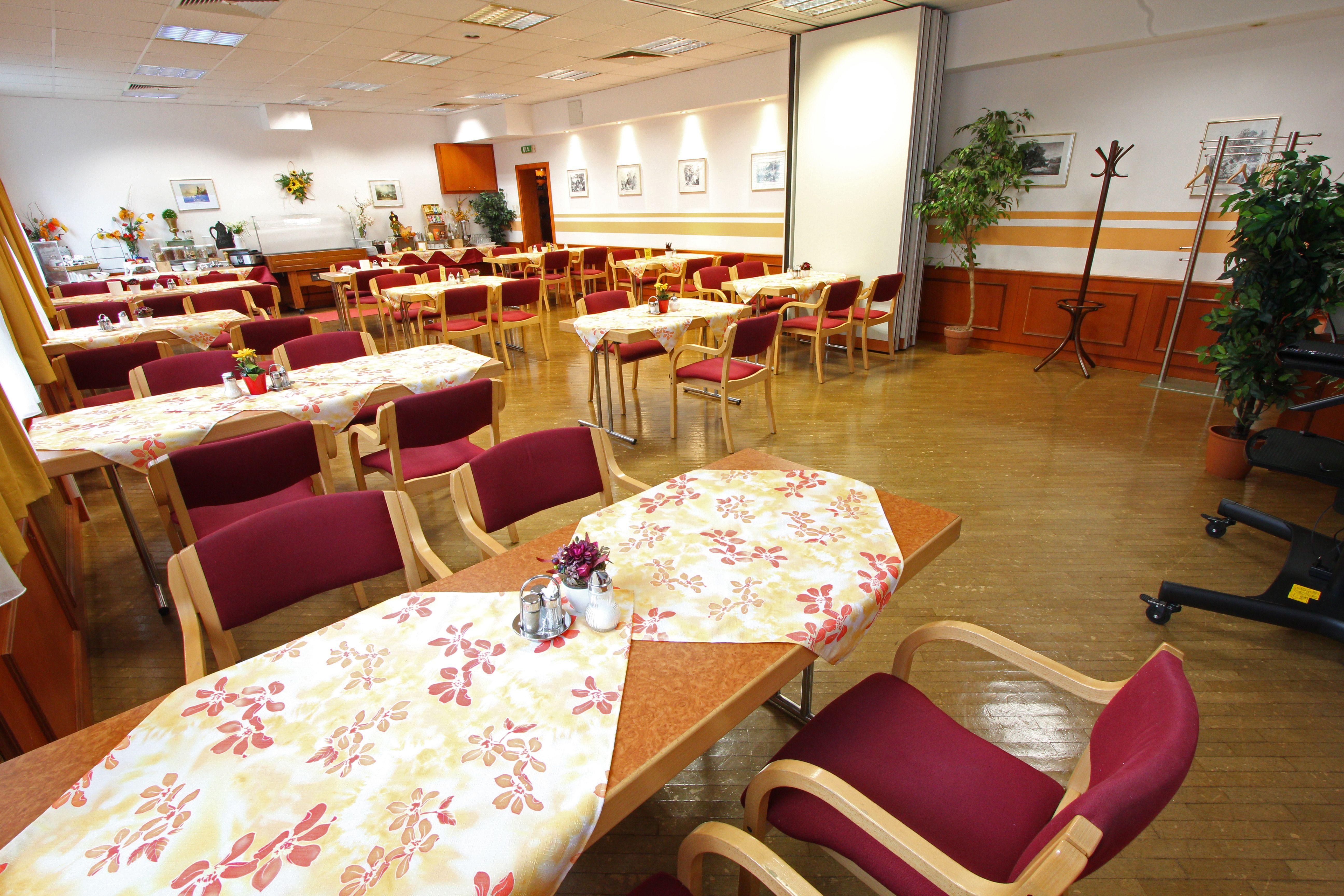 Ein leerer Speisesaal mit gedeckten Tischen und roten Stühlen.