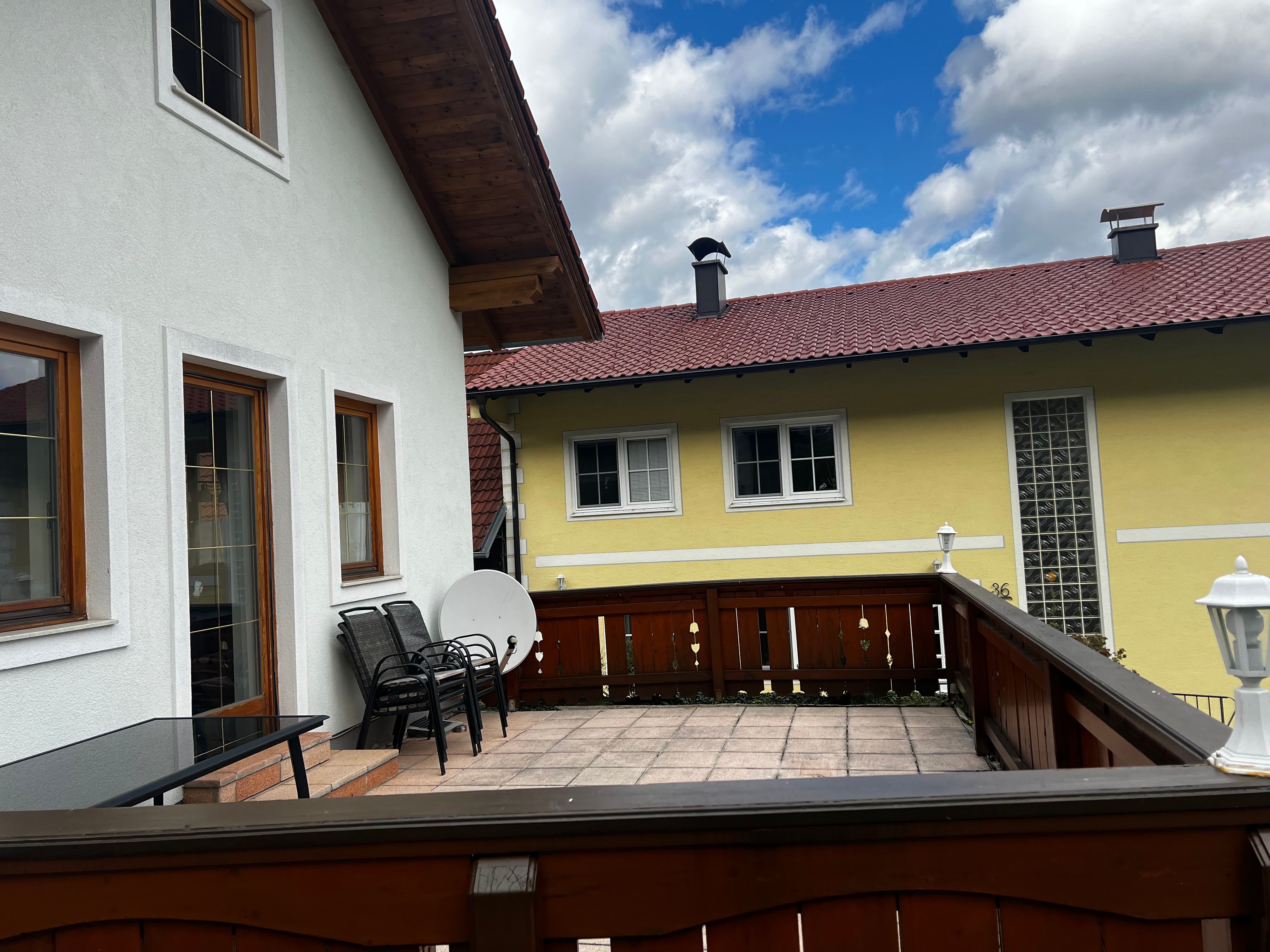 Terrasse eines Apartments mit Holzmöbeln und Blick auf ein gelbes Nachbarhaus mit rotem Dach.