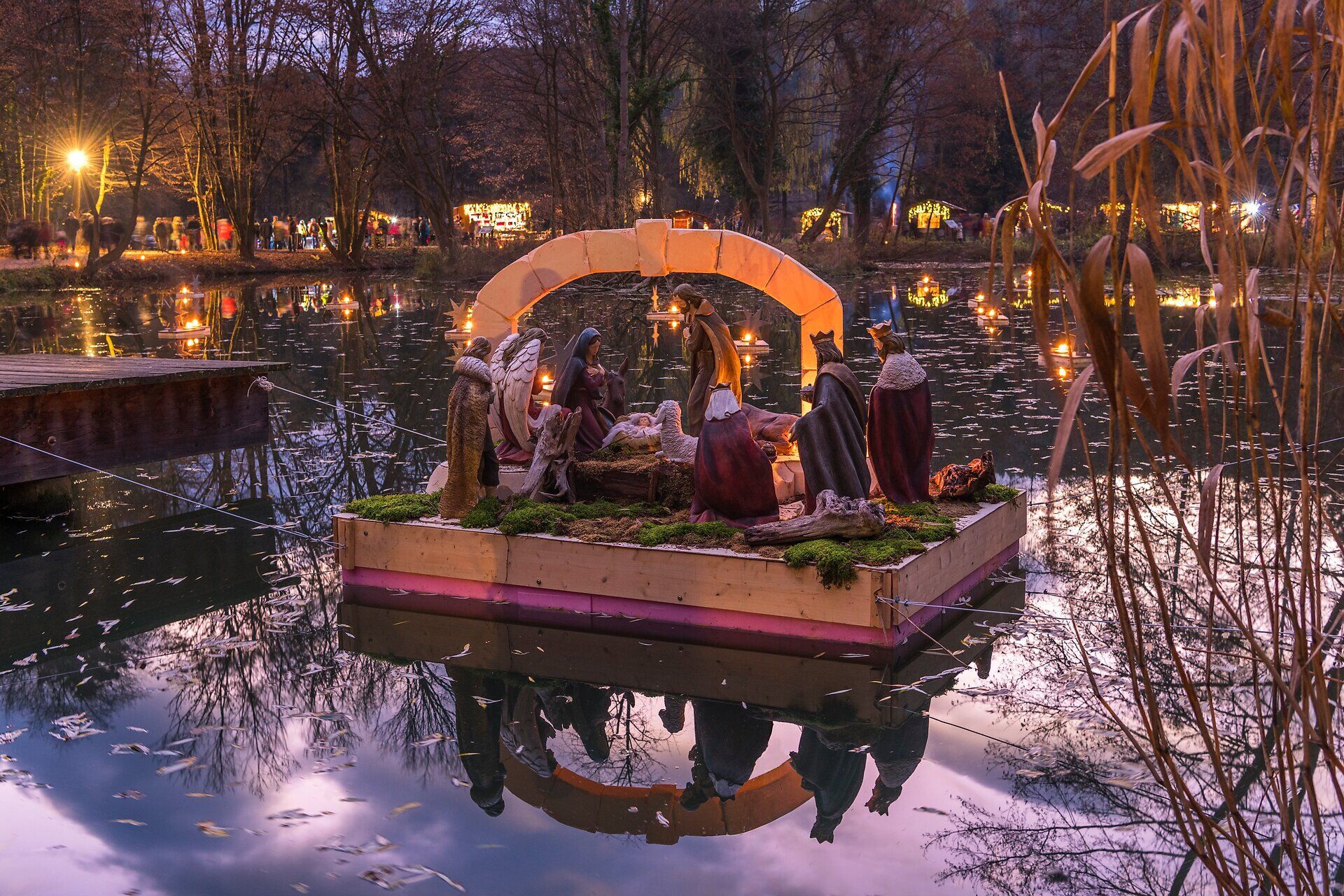 Schwimmende Krippenszene auf einem See, stimmungsvoll beleuchtet bei Abenddämmerung.
