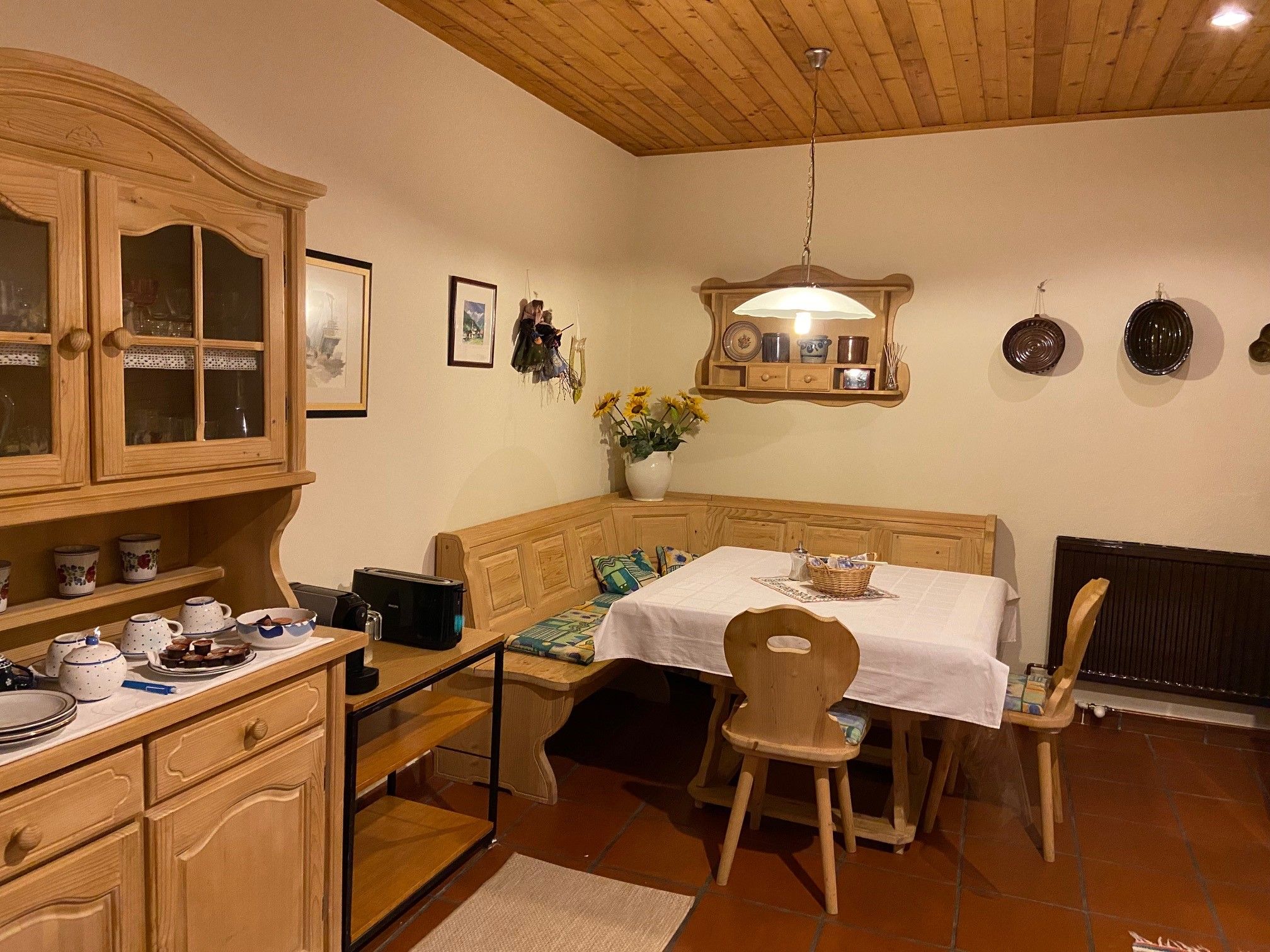 Gemütliche Küche mit Holzmöbeln, Esstisch und Eckbank, dekoriert mit Geschirr und Blumen.