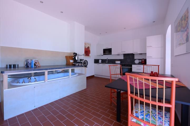 Moderne Küche mit weißen Schränken, Esstisch und roten Stühlen.