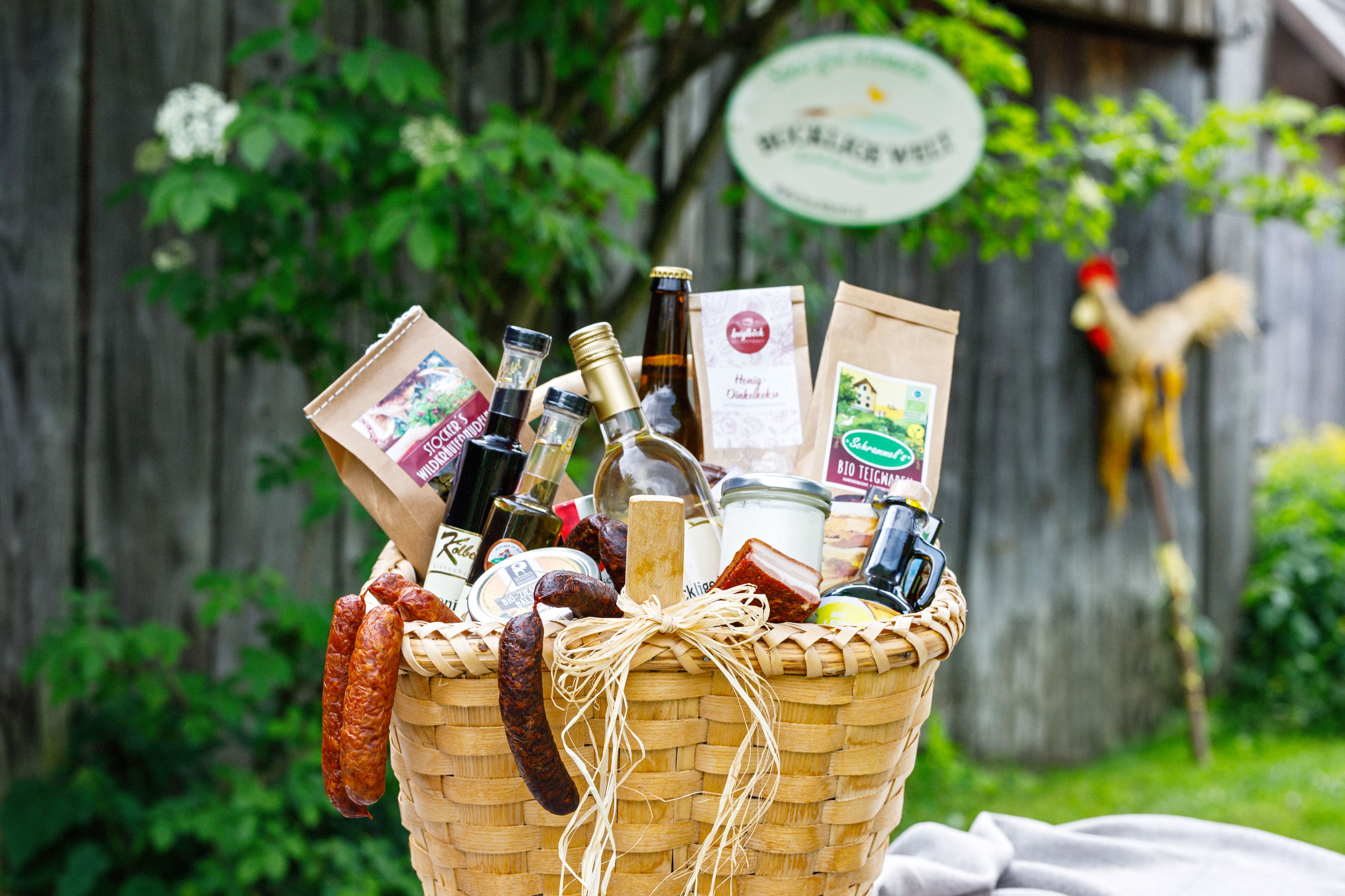 Geschenkkorb mit regionalen Lebensmitteln, im Hintergrund ein Holzzaun und ein Schnidahahn.