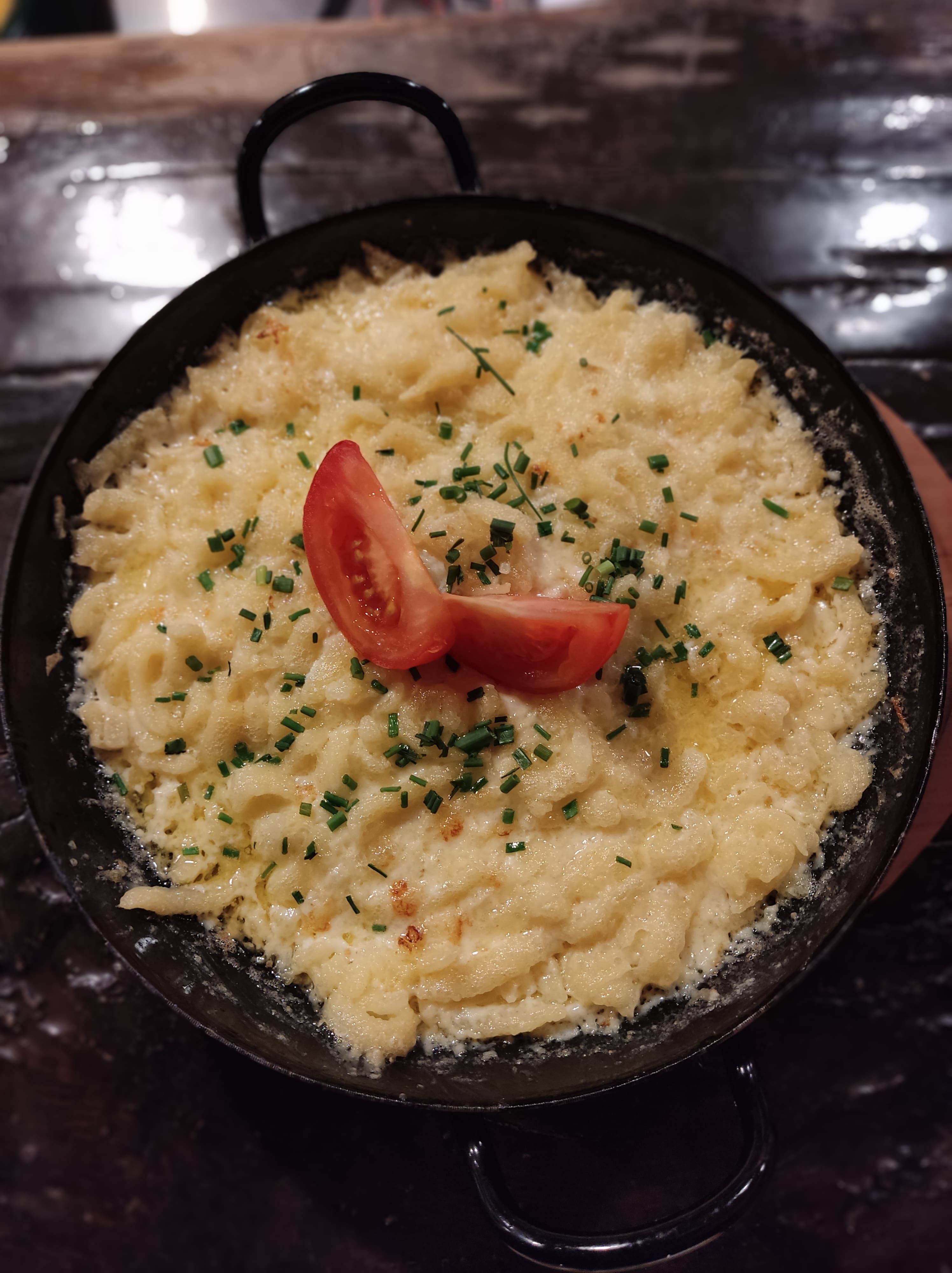Eine Pfanne mit Käsespätzle, garniert mit Tomaten und Schnittlauch.