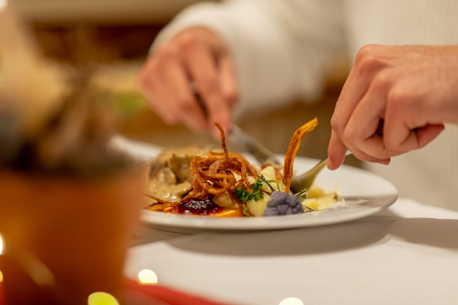 Nahaufnahme einer Tellers mit angerichteter Speise. Ein Mann hat Gabel und Messer in der Hand und beginnt zu essen.