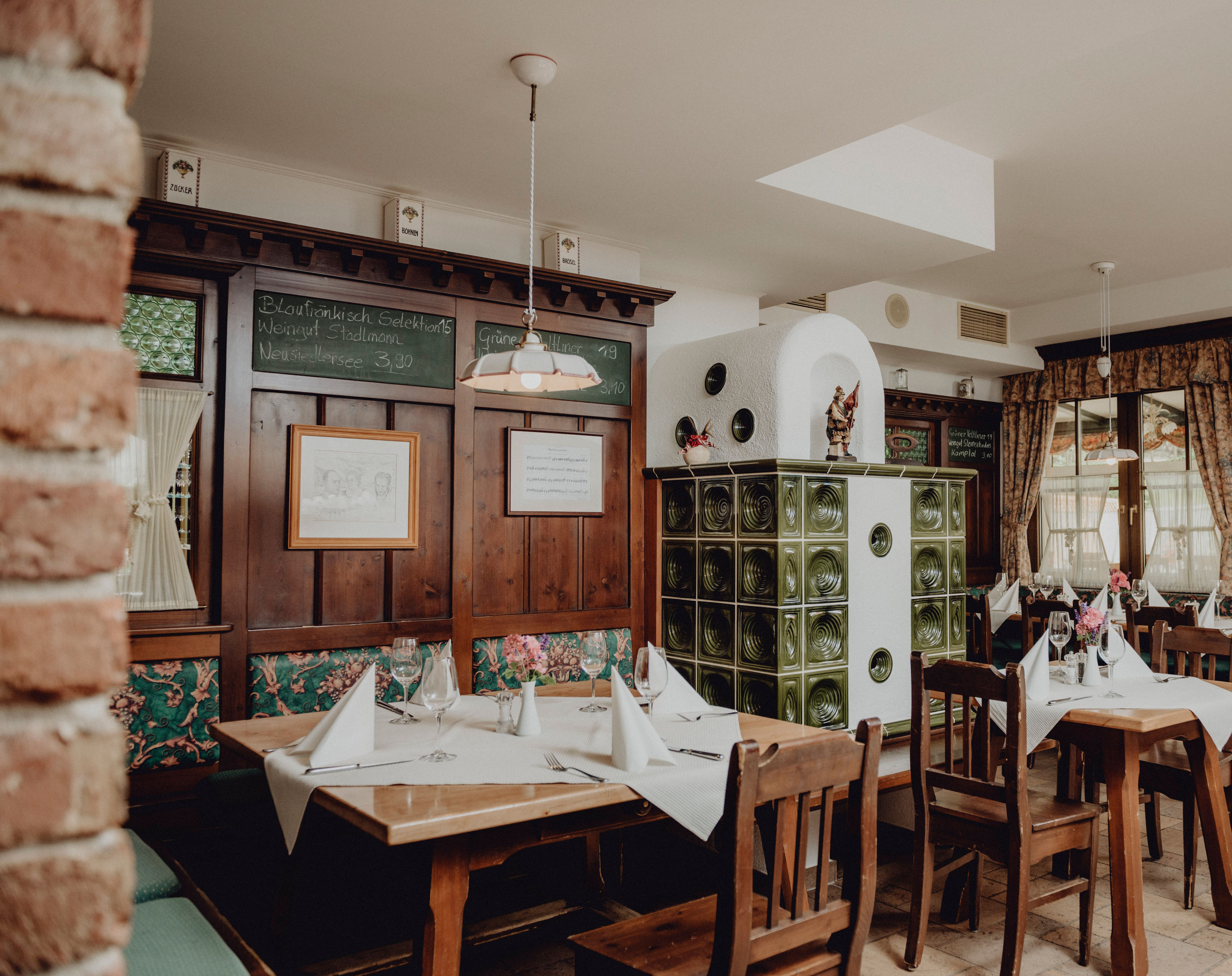 Ein Mann in einer Schürze kniet in einem Gemüsegarten und riecht an Kräutern, umgeben von grünen Pflanzen und einem Holzzaun.