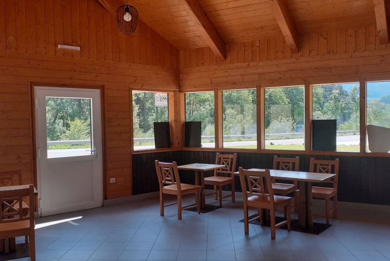 Interior view of a wooden building with tables and chairs, large windows and a door.