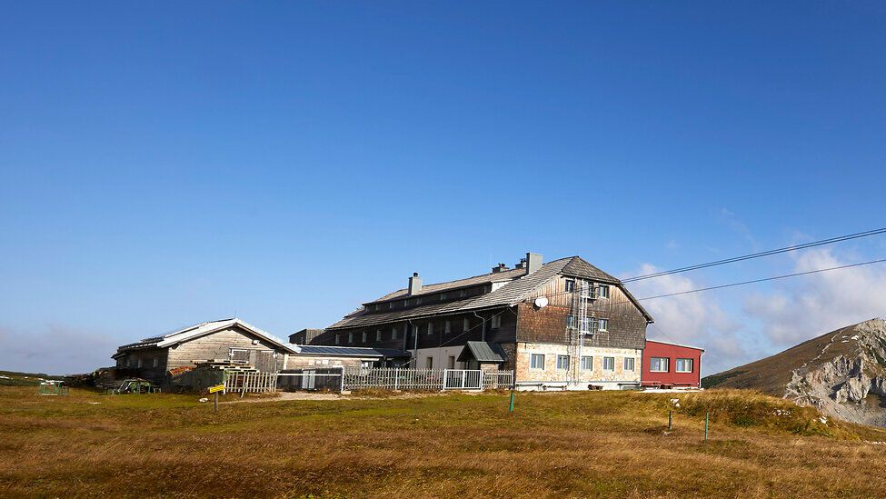 Panoramablick auf einen Berghütte mit umliegenden Gipfeln unter blauem Himmel.