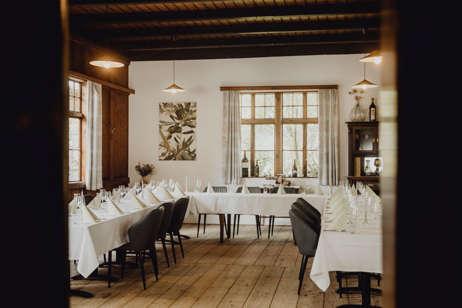 Eine gemütliche Gaststube mit weiß gedeckten Tischen, modernen Stühlen, Fenstern und Holzboden.