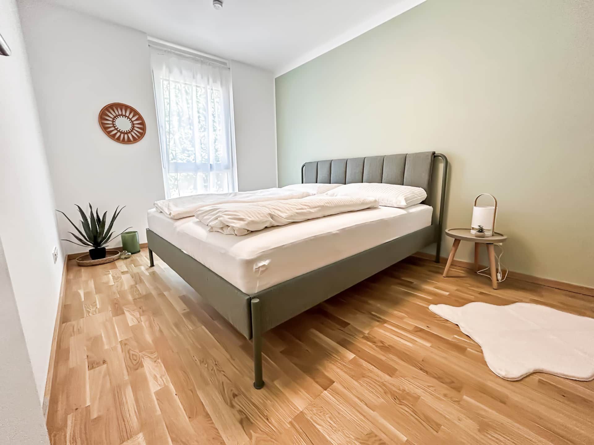 Large bedroom with double bed, carpet, large window and sage-green wall