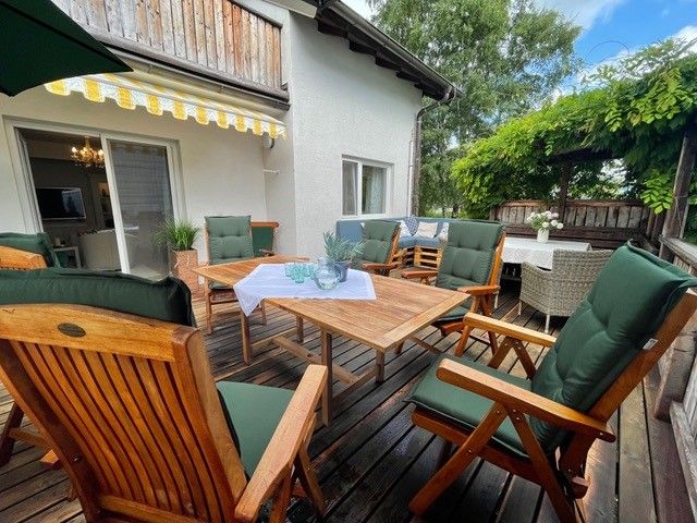 Holzterrasse mit Tisch, gemütlichen Stühlen und Sonnenschutz.