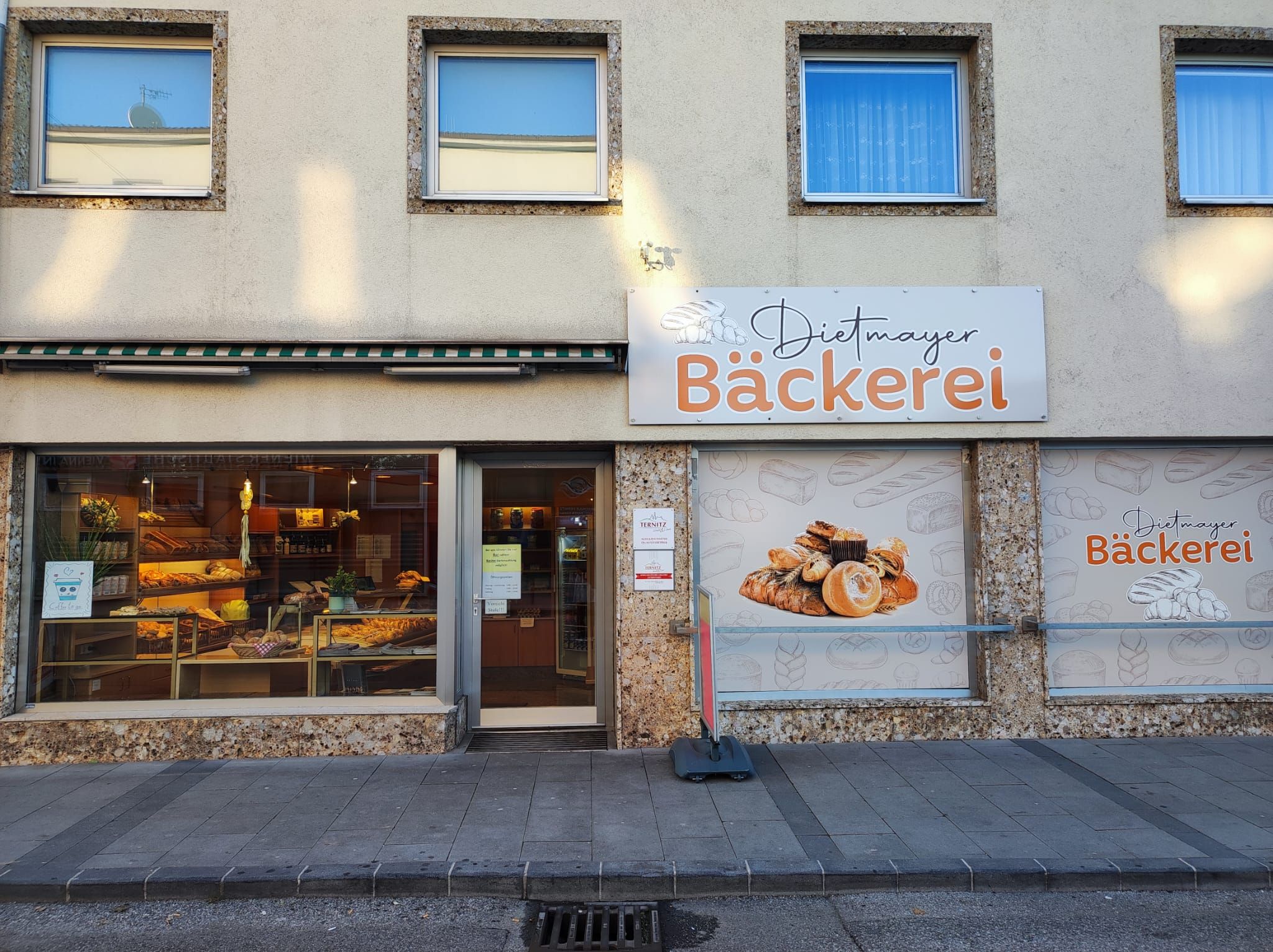 Fassade der Dietmayer Bäckerei in Ternitz mit Schaufenster, Eingang und großem Schild „Bäckerei“; im Inneren sind Backwaren zu sehen.