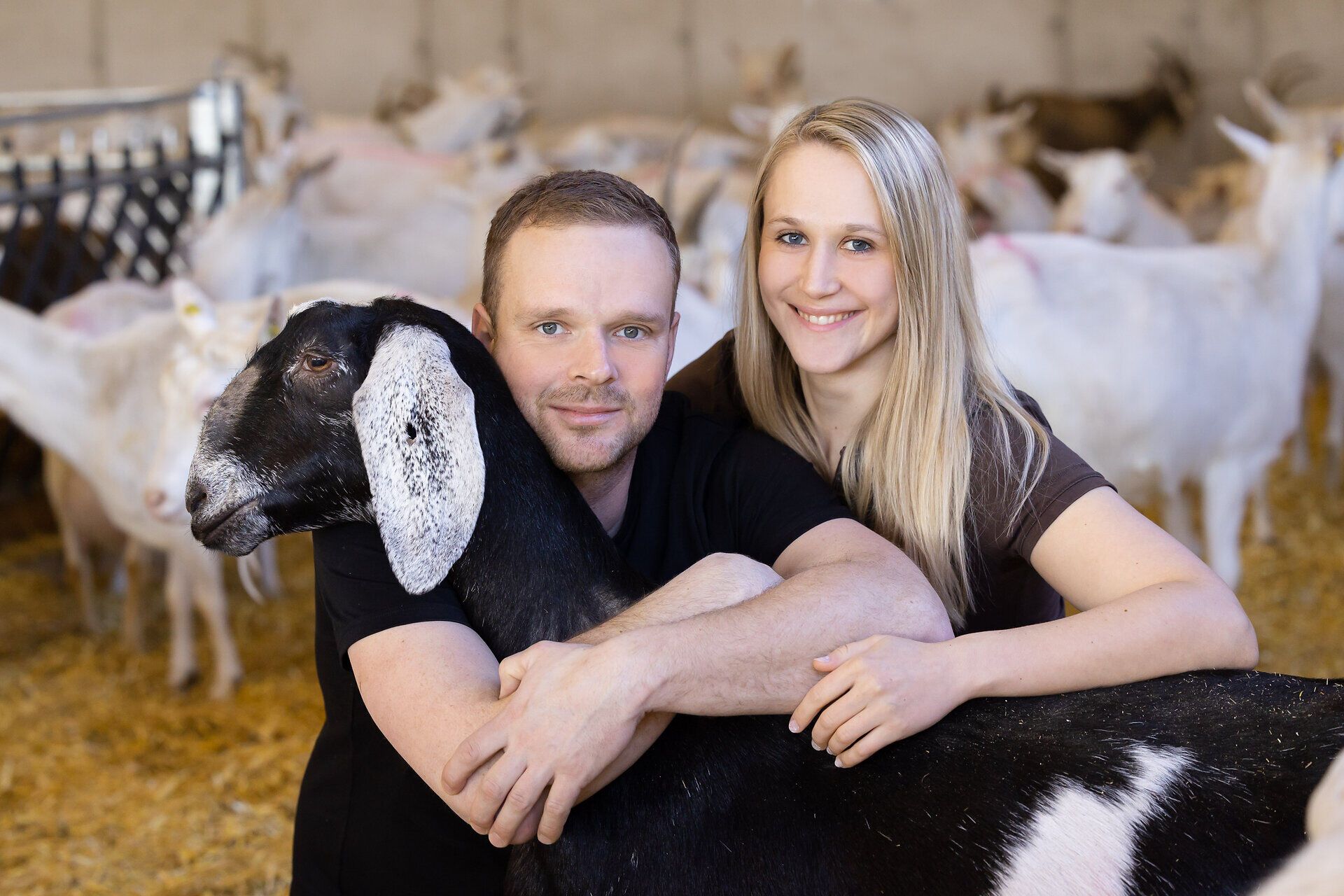 Inmitten einer idyllischen Ziegenfarm strahlen die Gesichter der beiden Menschen Freude und Verbundenheit aus. Umgeben von sanften Ziegen, die friedlich grasen, vermittelt die Szene ein Gefühl von Harmonie und ländlicher Idylle. Hier wird die Liebe zur Natur und zu den Tieren spürbar.
