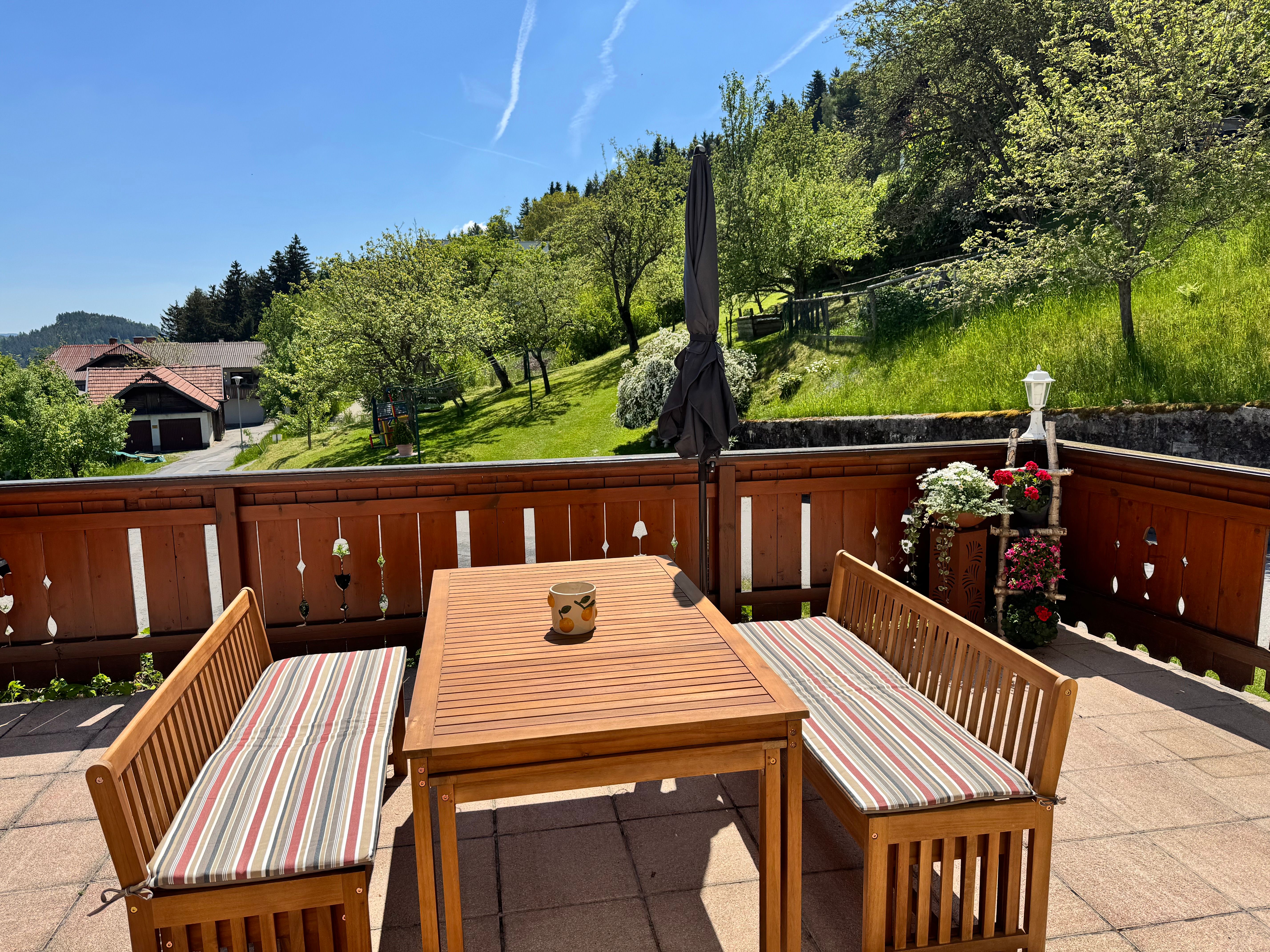 Terrasse mit Holzmöbeln und Blick auf grüne Wiesen und Bäume.