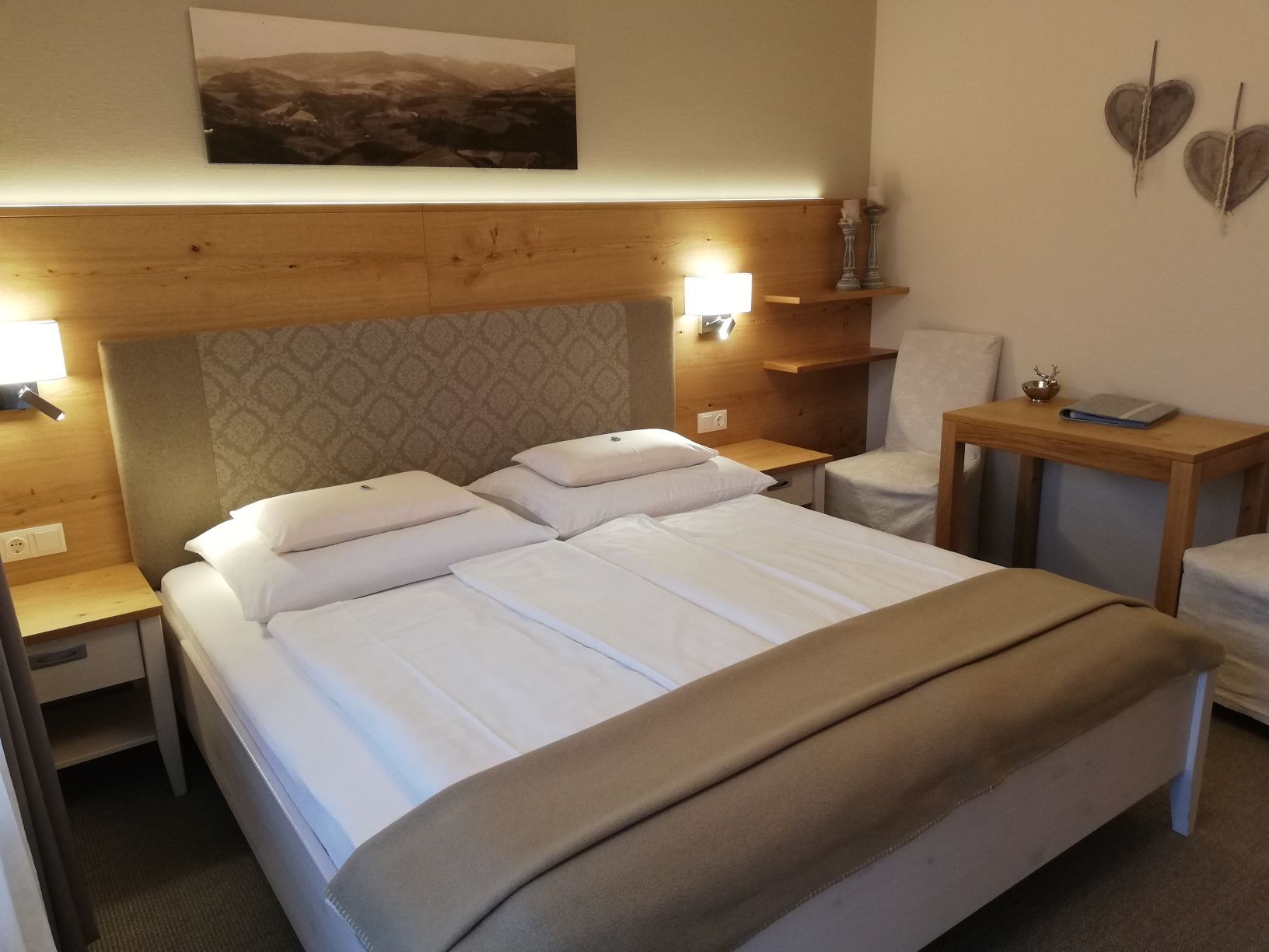 Gemütliches Hotelzimmer mit Doppelbett, Holzmöbeln und Wanddekoration.