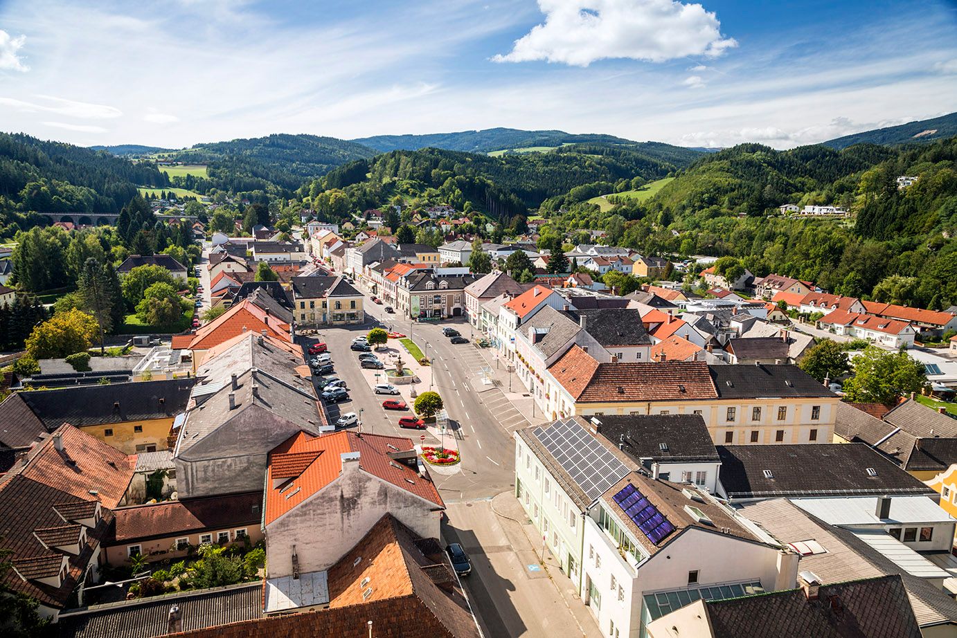 Luftaufnahme von Aspang Markt mit roten Dächern und grüner Landschaft im Hintergrund.