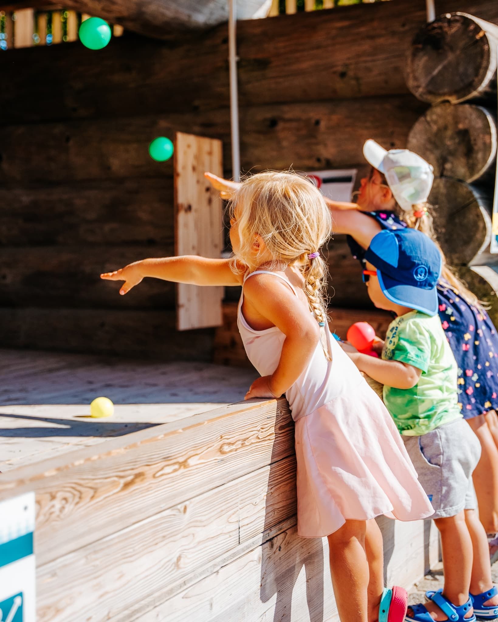 Drei Kinder werfen bunte Bälle in einen Holzstand.