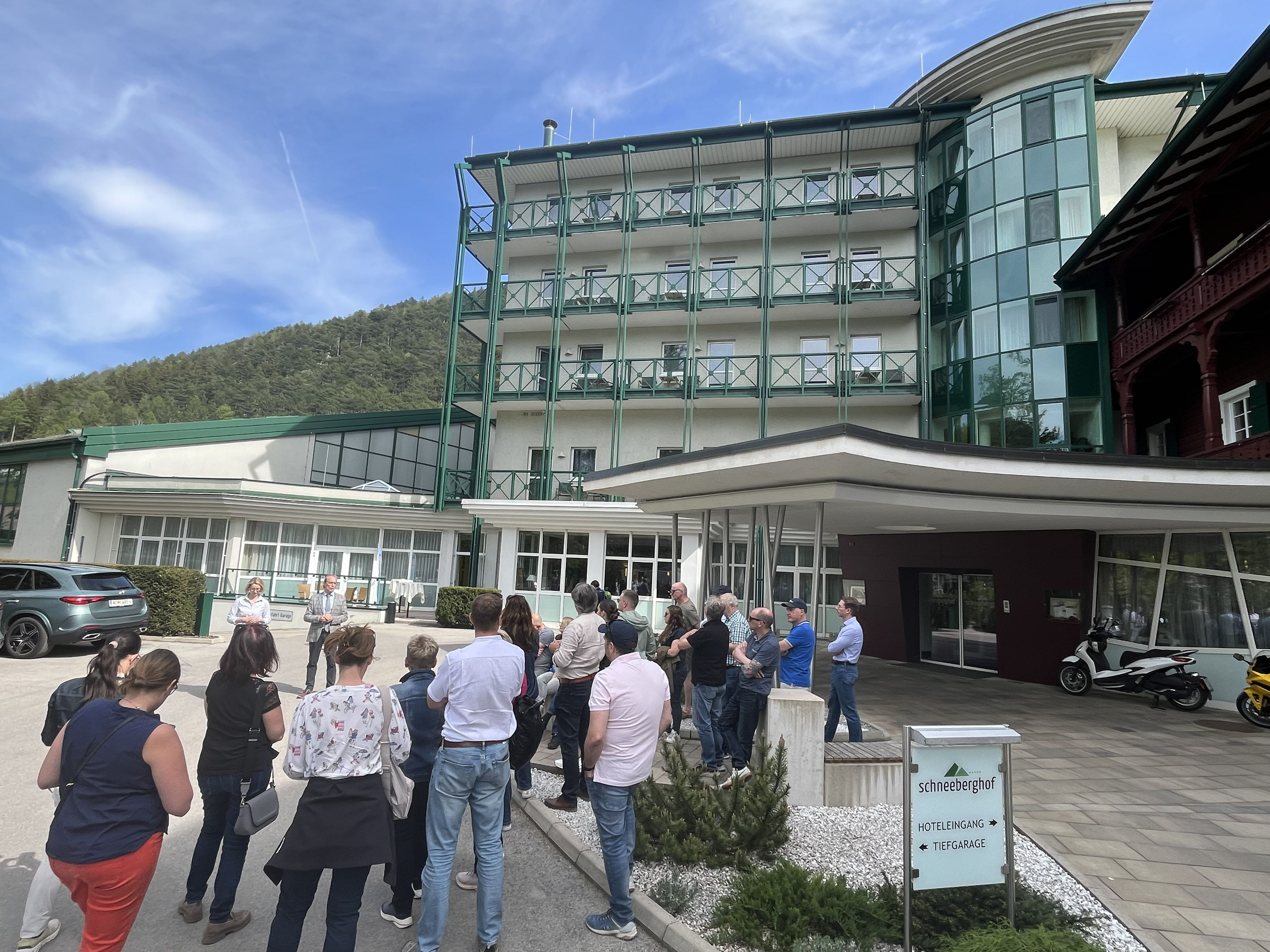 Zwei Personen sprechen vor einer Gruppe von rund 20 Personen vor dem Schneeberghof. 