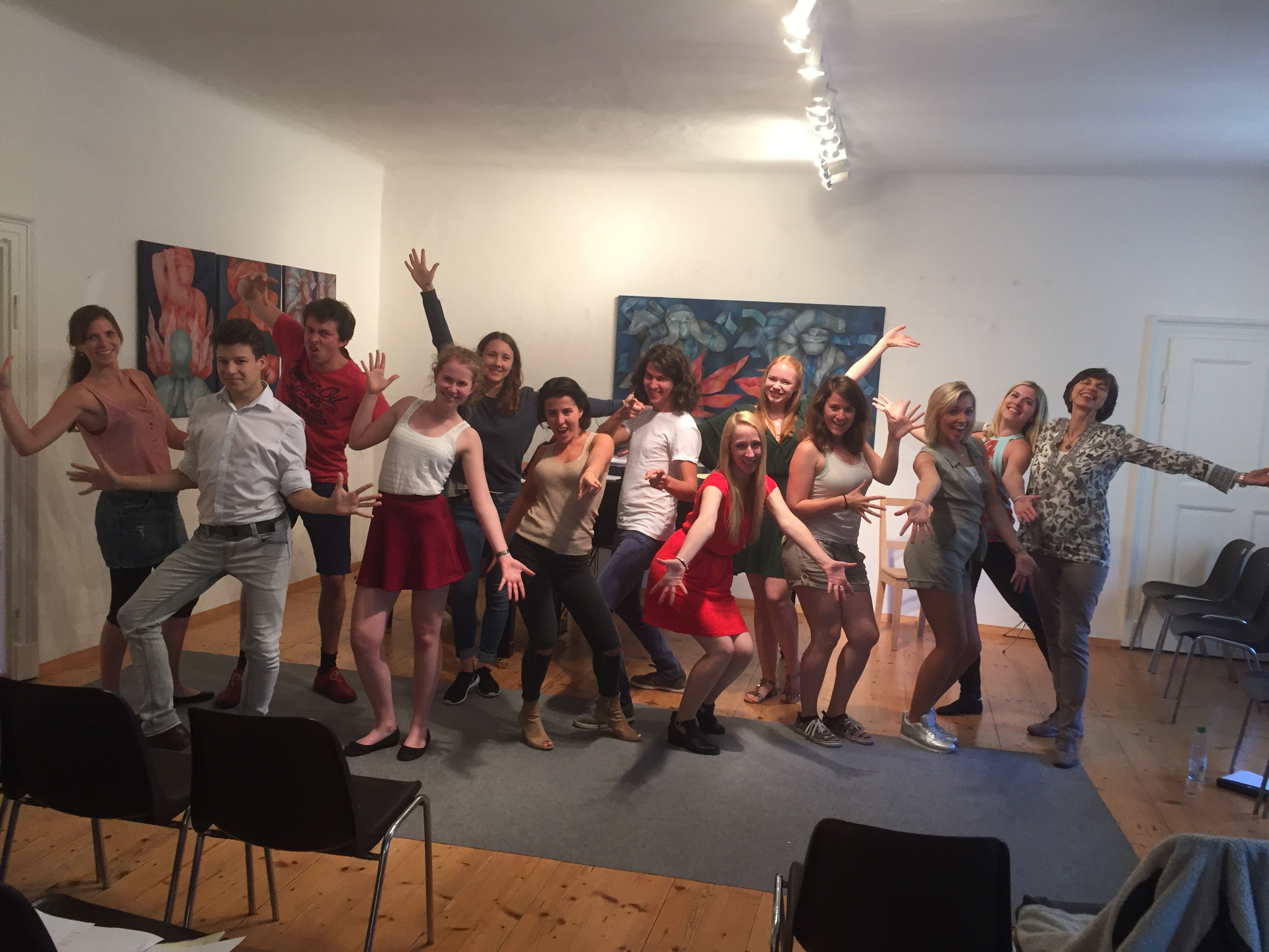 Eine Gruppe von Menschen posiert fröhlich in einem Raum mit Holzboden und Kunstwerken an der Wand.