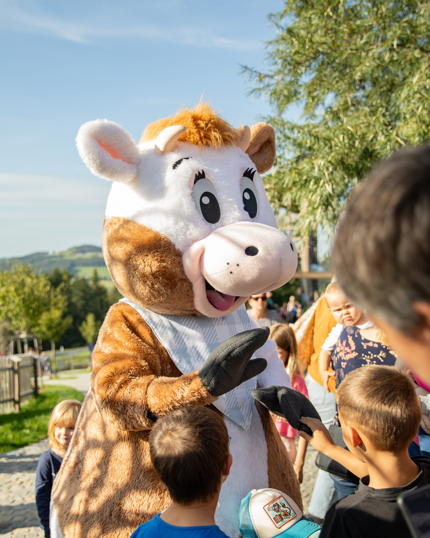 Ein Kuh-Maskottchen steht in einem Erlebnispark und interagiert mit Kindern.