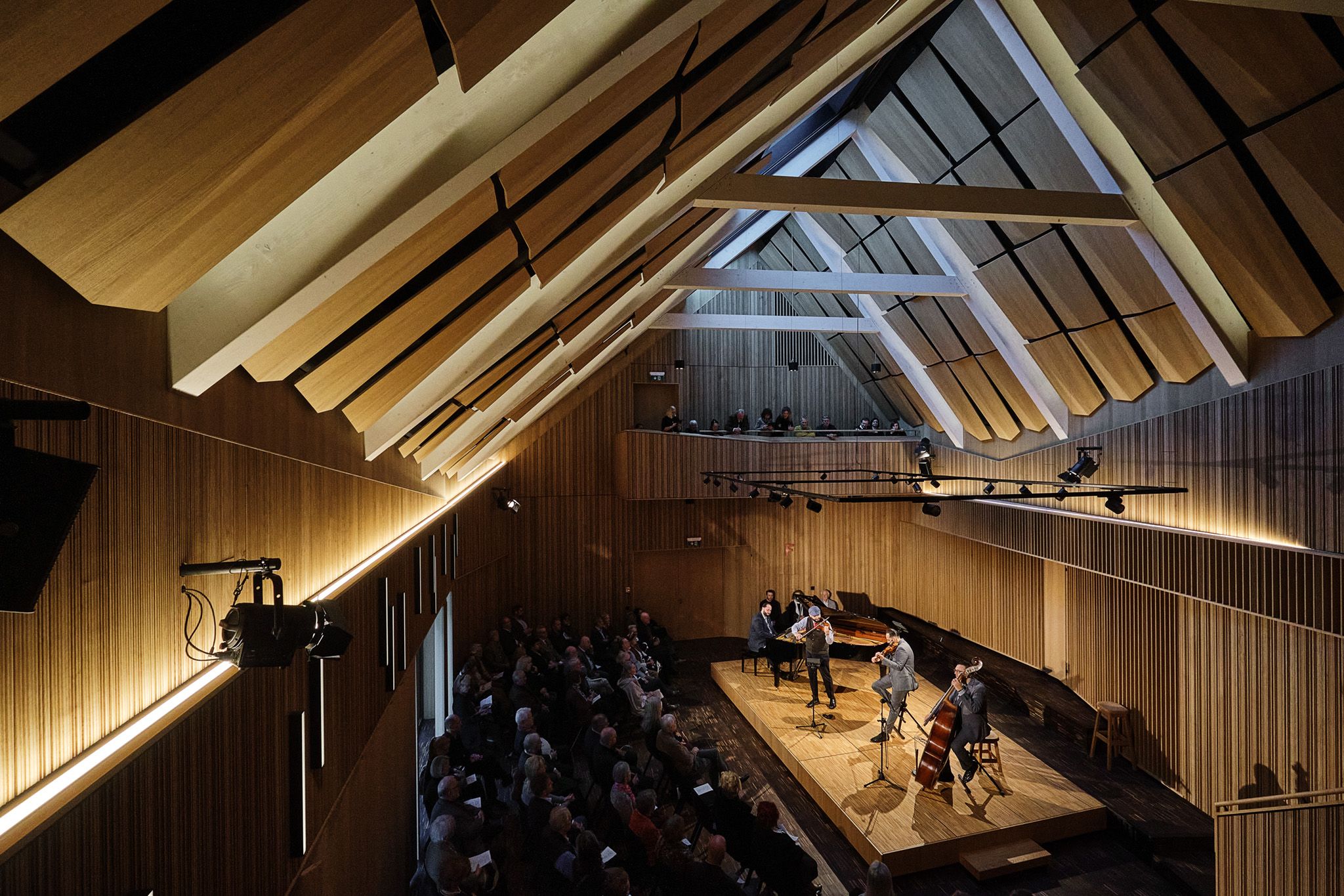 Interior view of a modern concert hall with wooden paneling and musicians on stage.