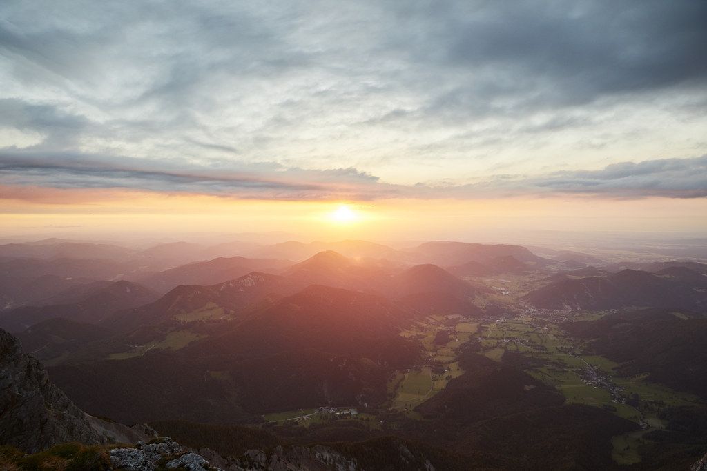 Sonnenuntergang über einer Berglandschaft mit Wolken und Tälern.