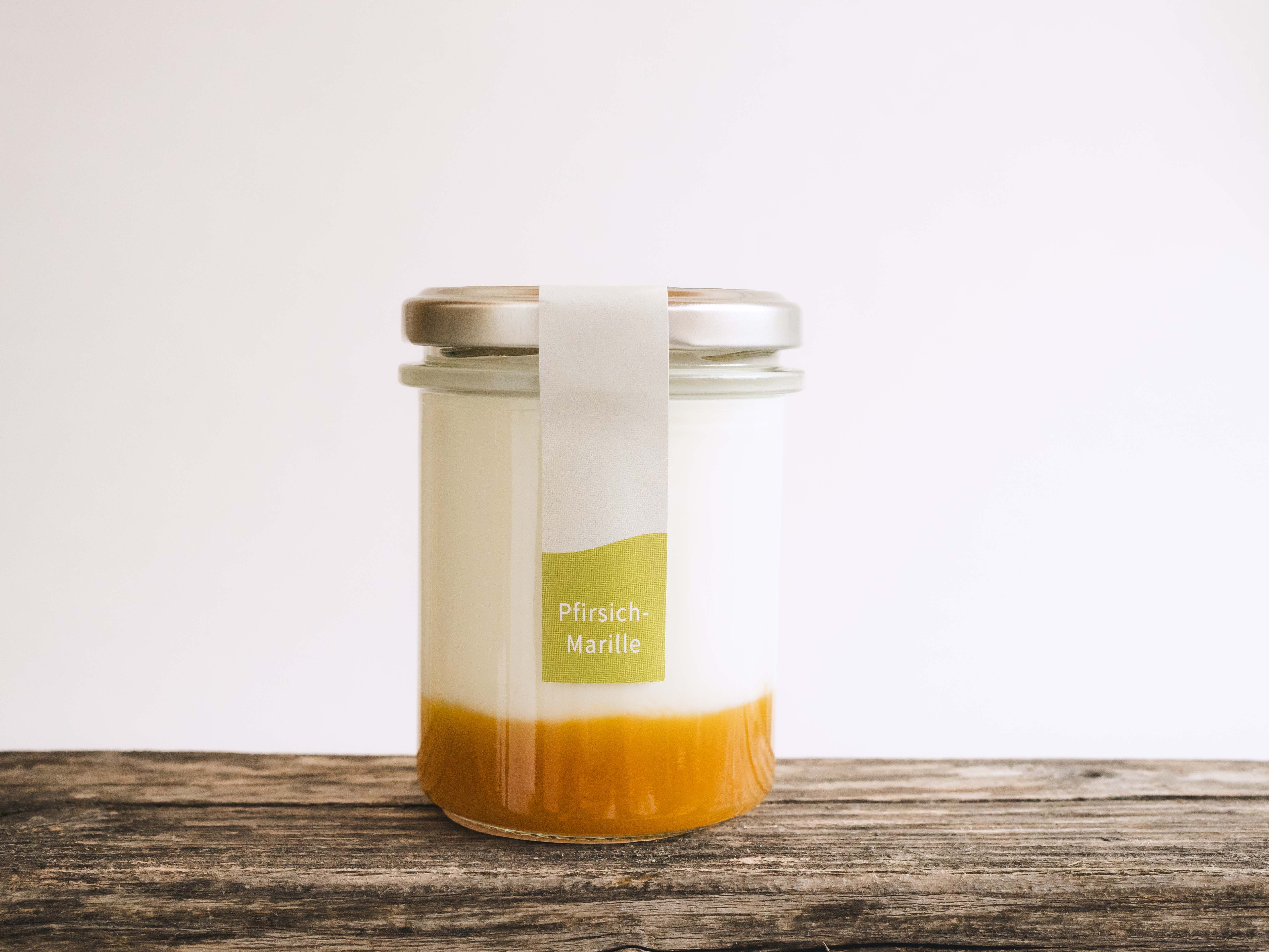 Ein Glas mit Pfirsich-Marillen-Fruchtspiegel und Naturjoghurt auf Holzboden.