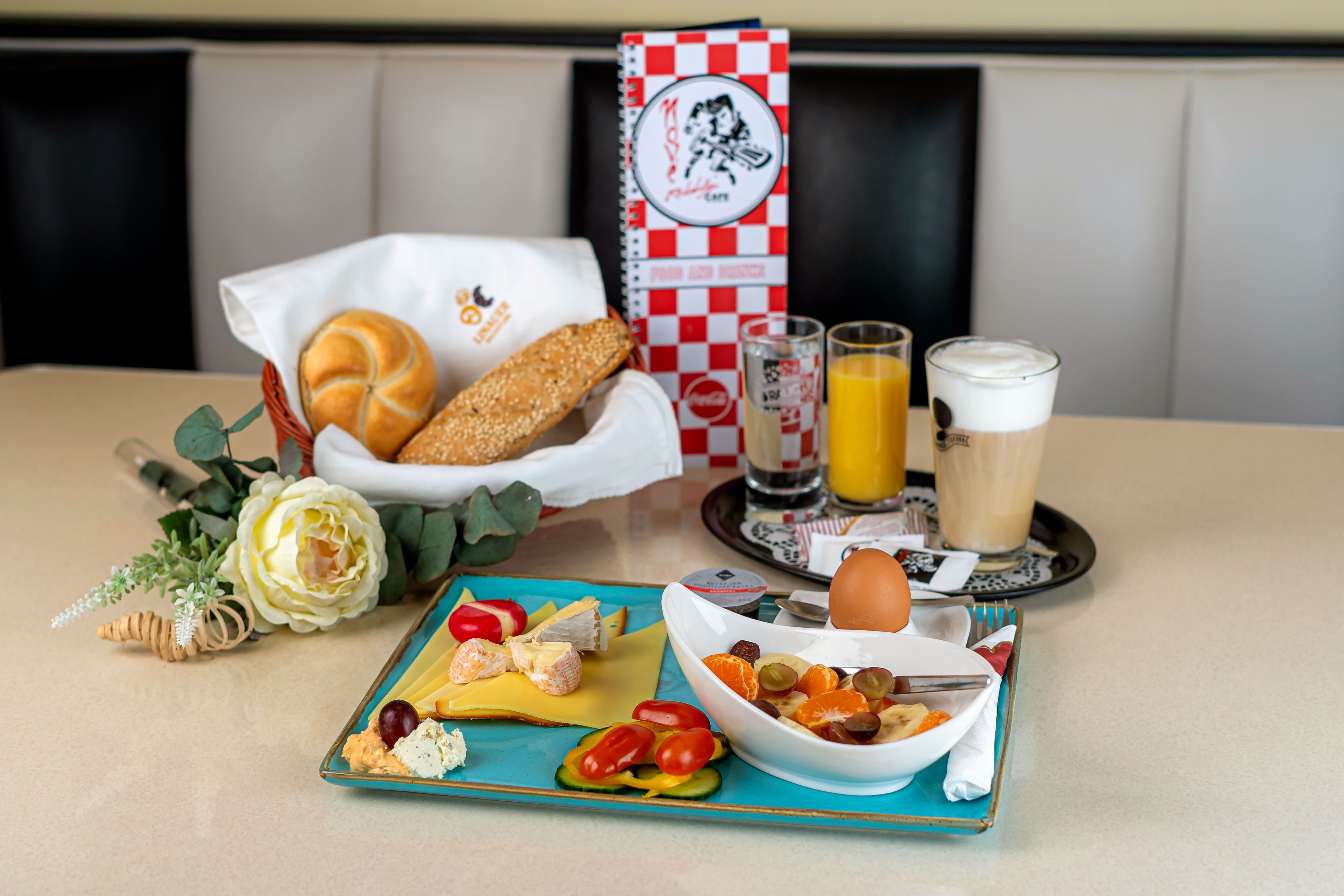 Frühstückstisch mit Brötchen, Käse, Obst, Ei, Saft und Kaffee in einem Café.