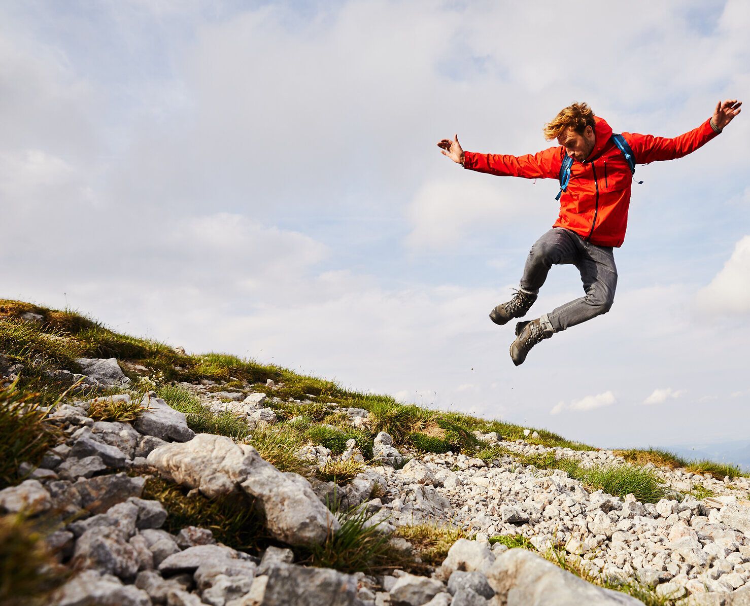 Ein abenteuerlustiger Wanderer springt voller Freude über die felsige Landschaft des Schneebergs. Die frische Bergluft und die atemberaubende Aussicht auf die Wiener Alpen schaffen eine unvergessliche Atmosphäre für Naturliebhaber und Abenteurer.
