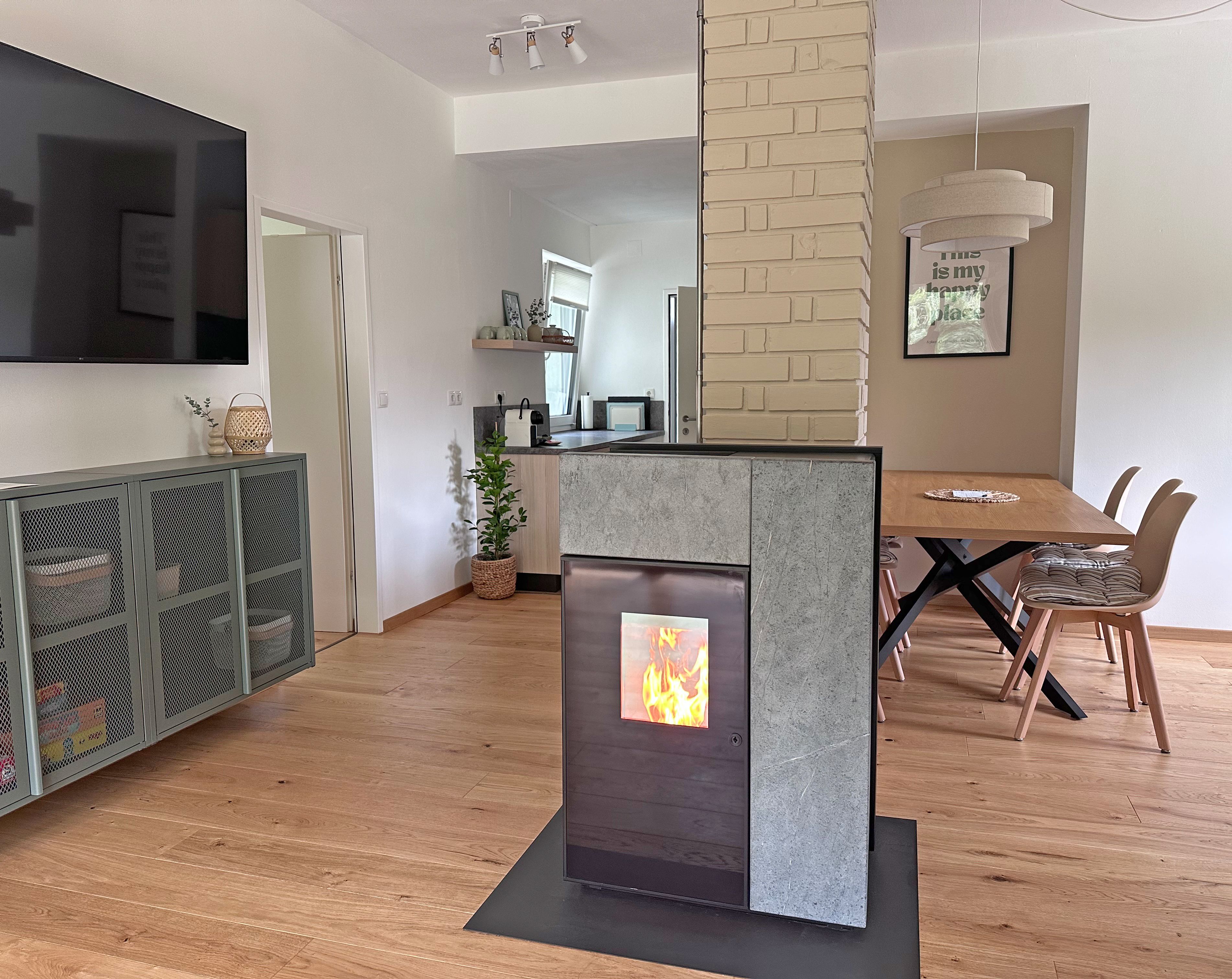 Modern living and dining room with a wood-burning stove, hardwood floors, a dining table, and a TV mounted on the wall.