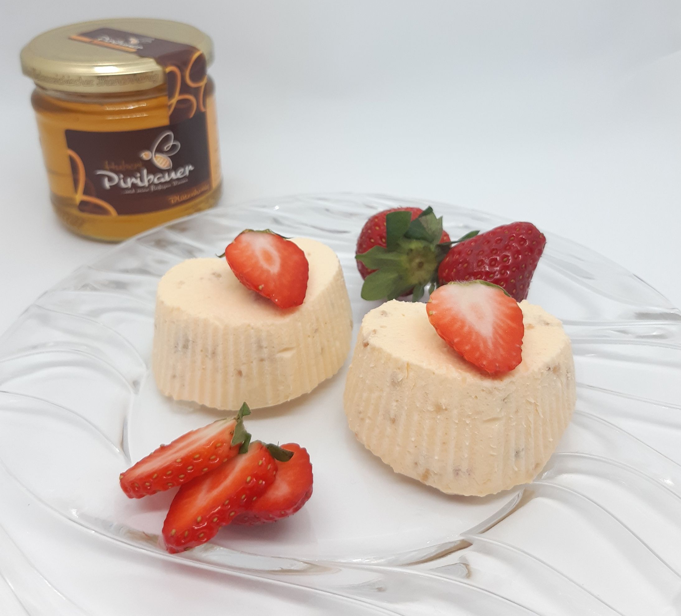 Zwei geeiste Honigherzen auf Glasteller, ganiert mit Erdbeeren. Im Hintergrund ein Honigglas.