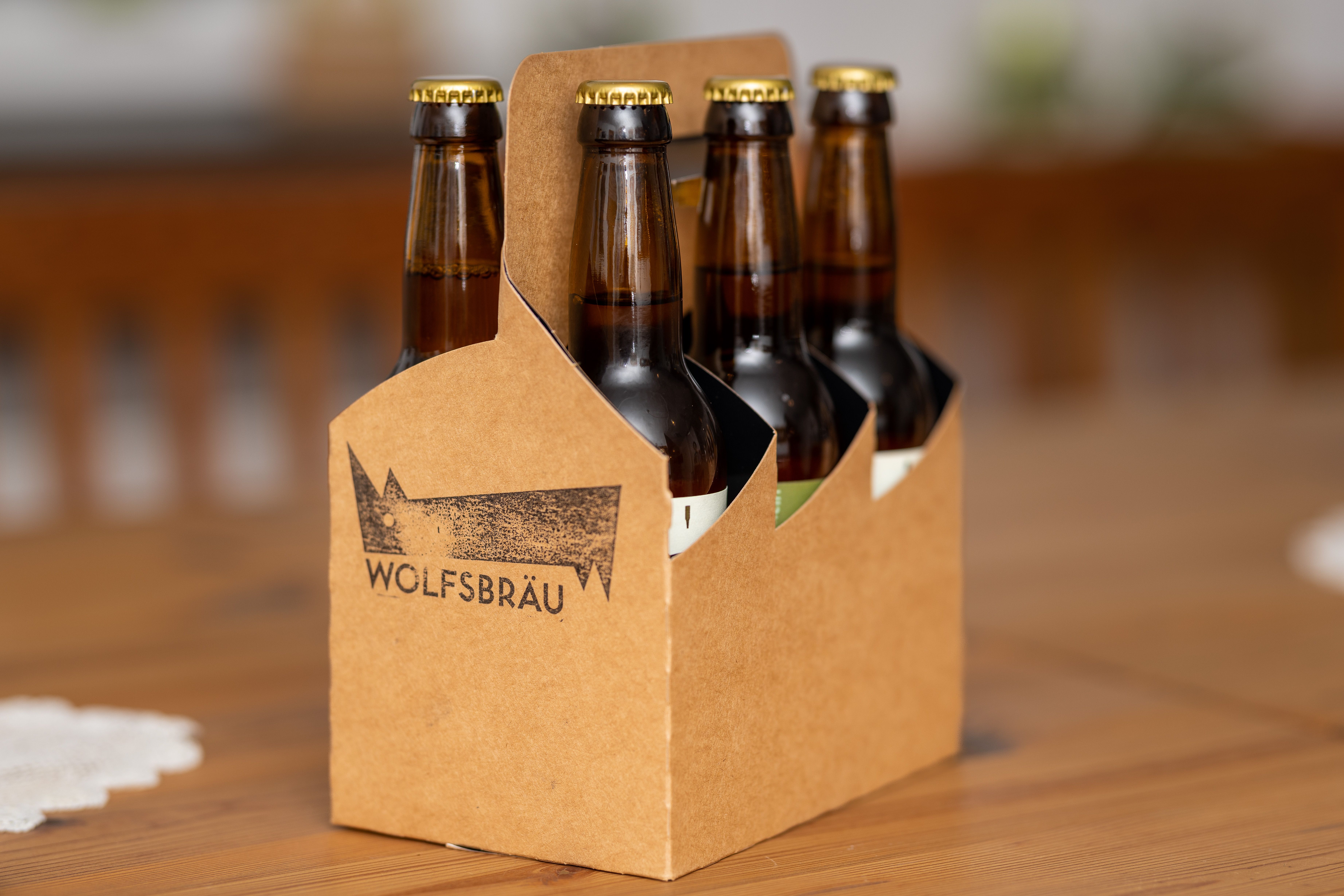 Eine Papiertrage mit sechs braunen Bierflaschen auf einem Holztisch.