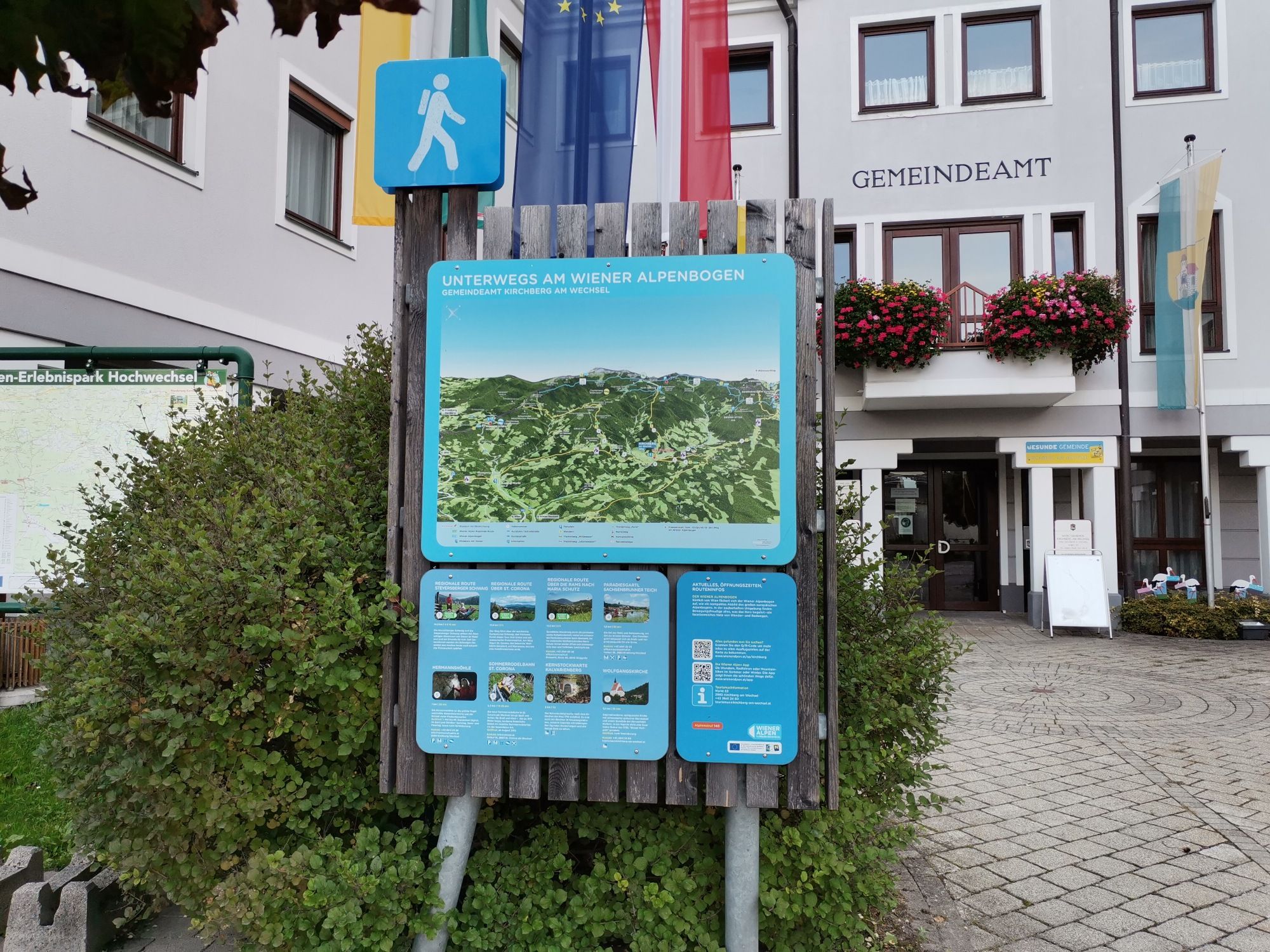 Wanderkarte vor dem Gemeindeamt Kirchberg am Wechsel mit Hinweisschildern und Flaggen.