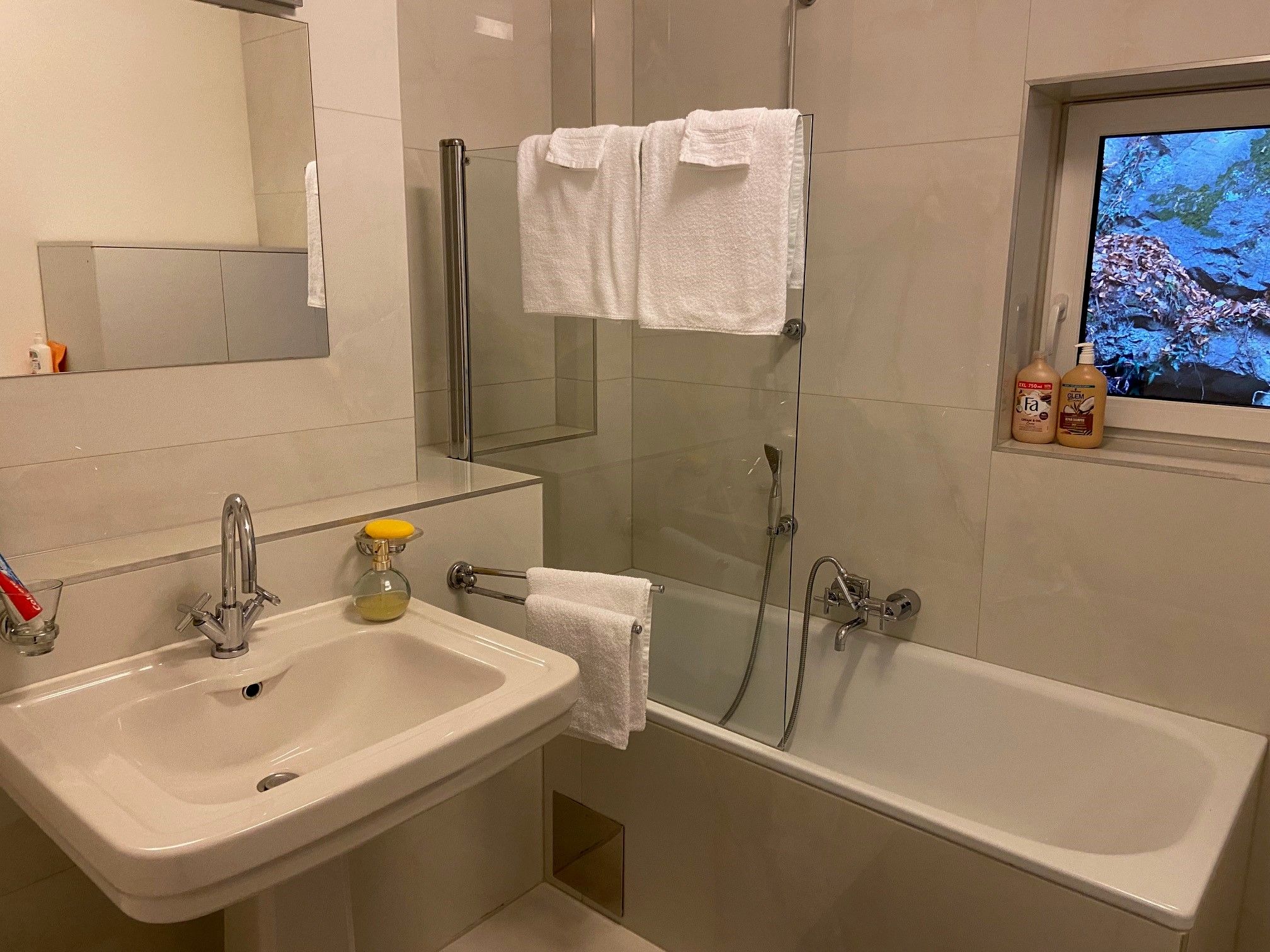 Modernes Badezimmer mit Waschbecken, Spiegel, Badewanne und Handtüchern.