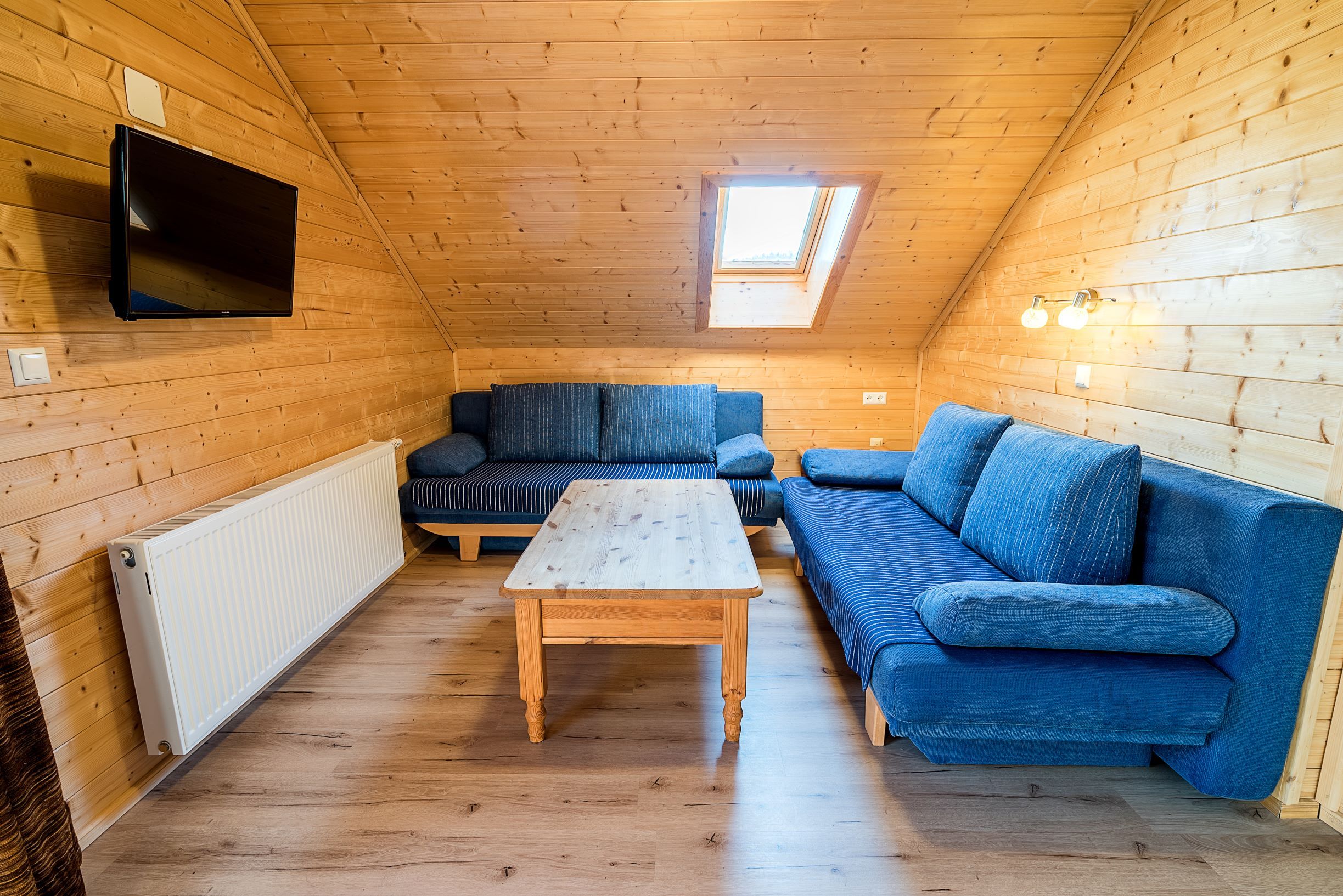 Wohnzimmer mit Holzwänden, blauen Sofas, Holztisch und Dachfenster.