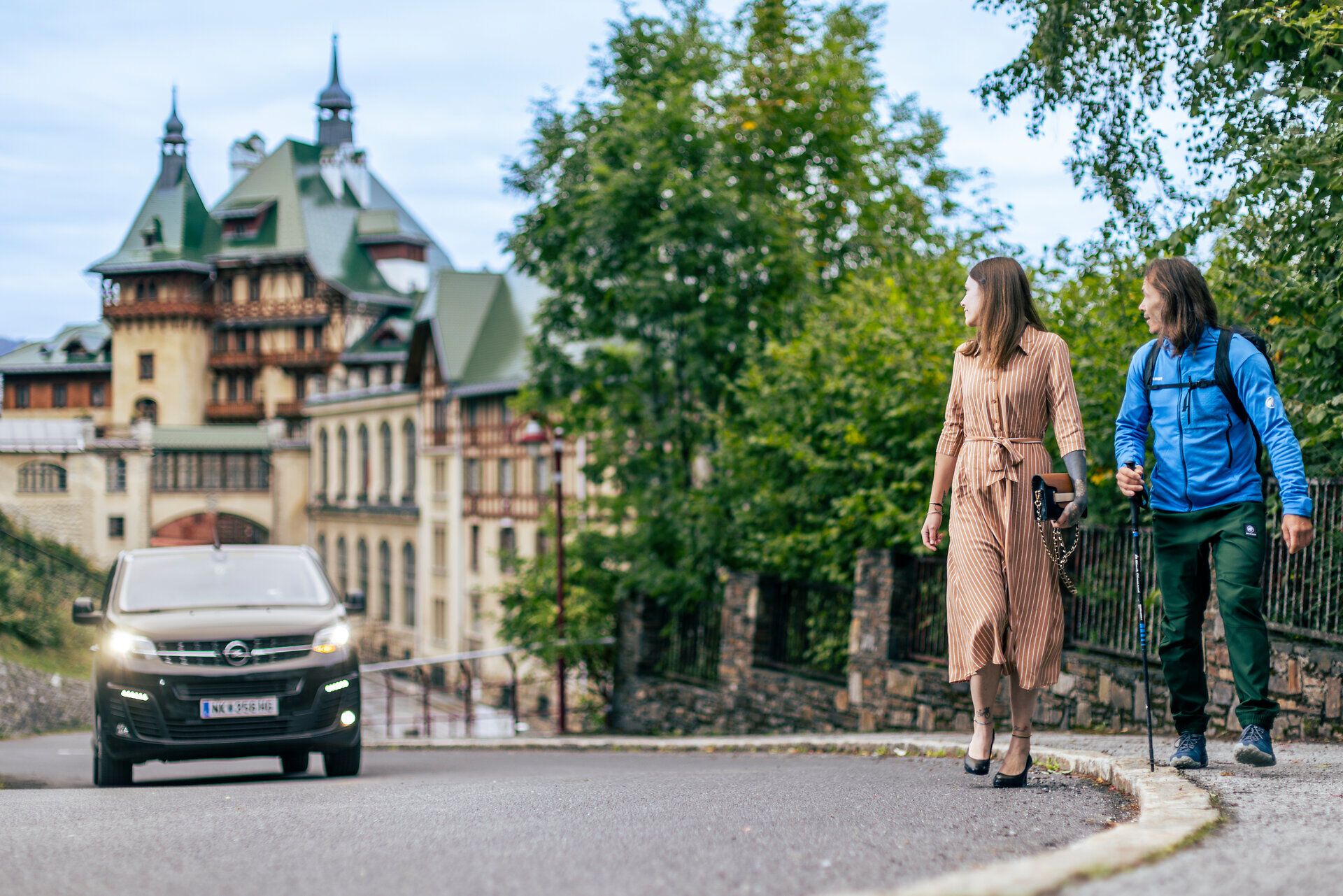 Ein schwarzer Kleinbus, der RUF Bus, holt gerade eine Frau in einem schönen orangen Kleid und einen Wanderer ab. 