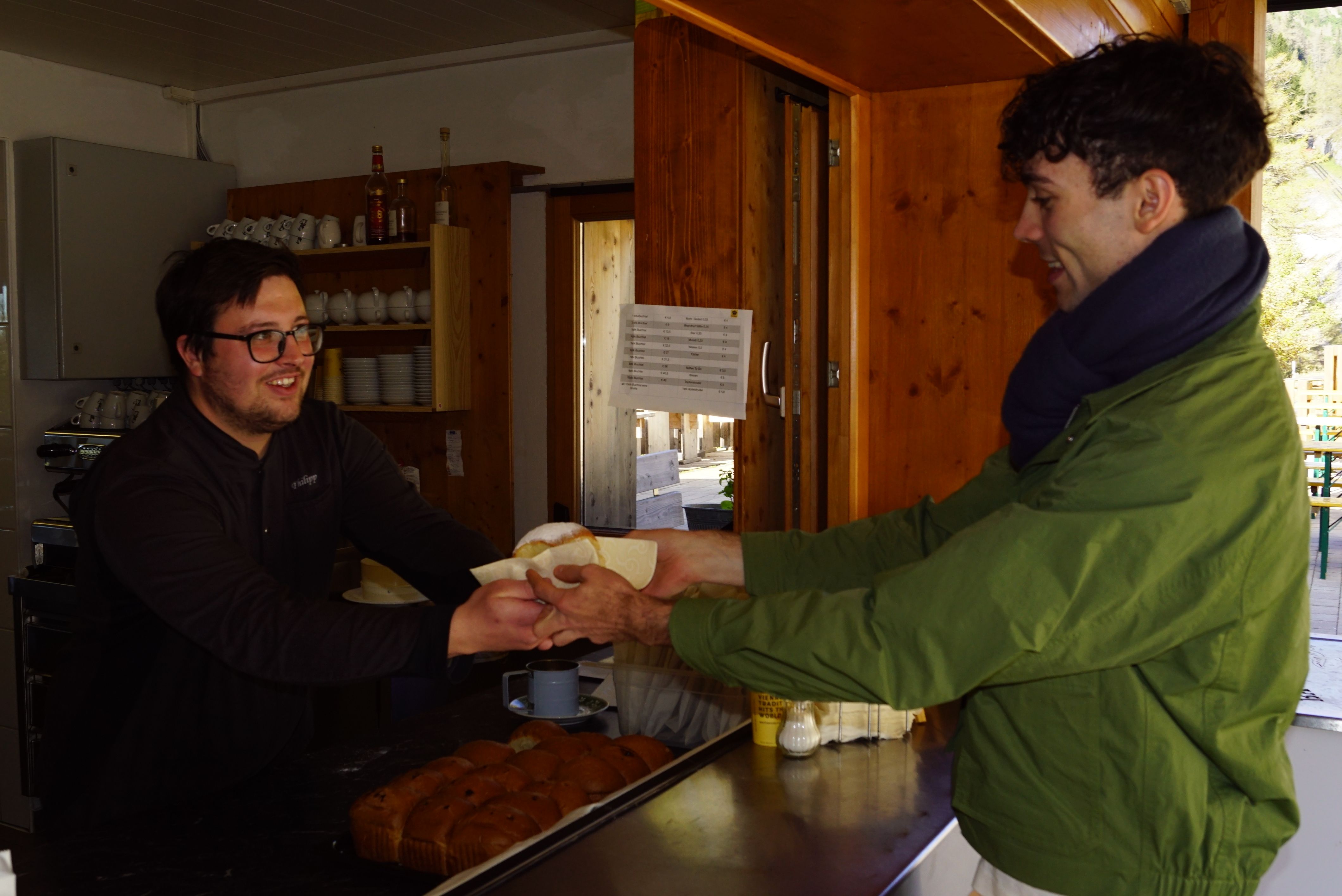 Bei Dreharbeiten nimmt der Darsteller eine Serviette mit Buchtl durch ein offenes Fenster von einem Mann entgegen.
