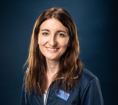 Portraitfoto Wiener Alpen Mitarbeiterin, die eine Jacke mit Wiener Alpen Logo trägt und vor einem dunklem Hintergrund steht.