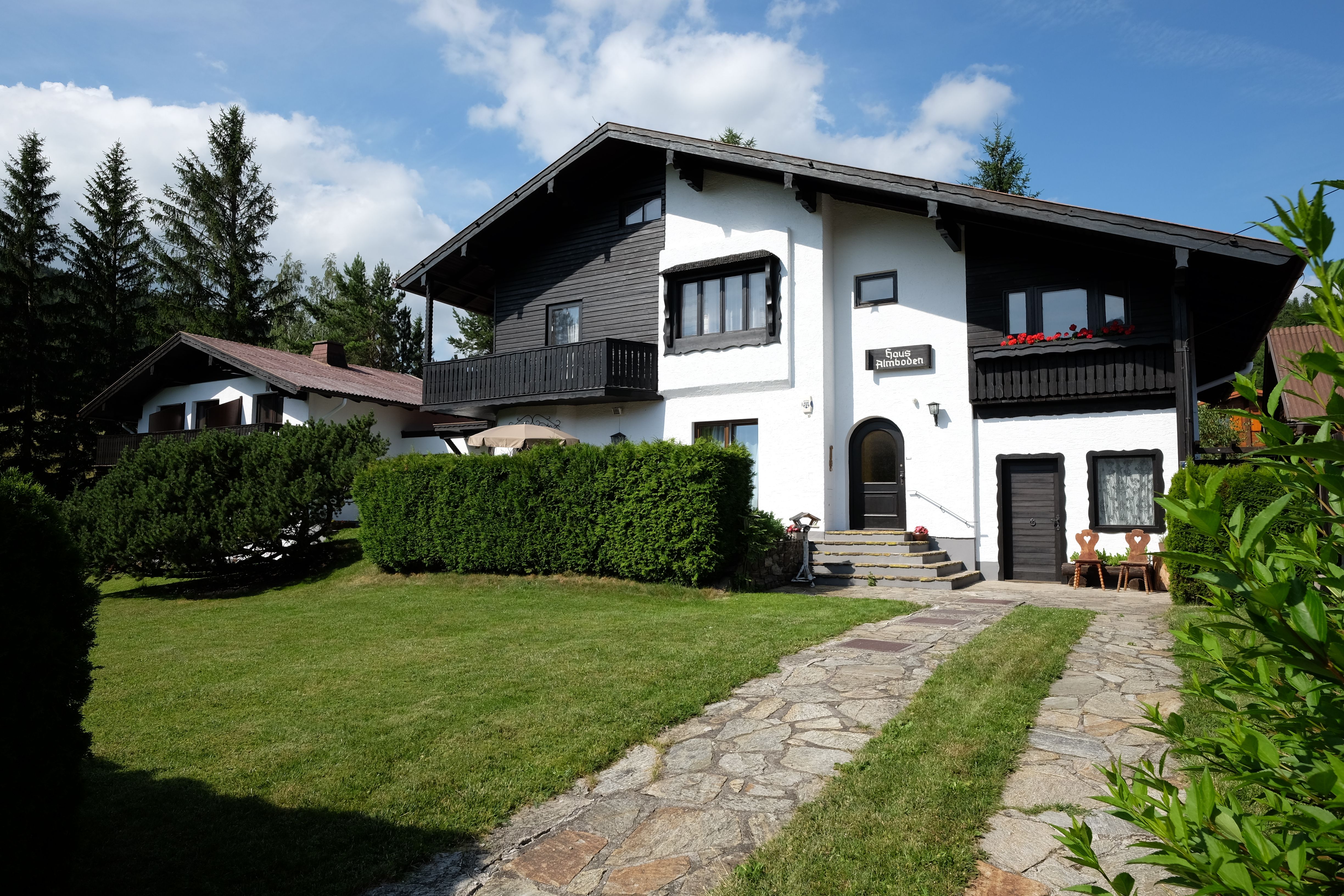 Ein zweistöckiges Haus mit schwarzem Holz und weißen Wänden, umgeben von einem gepflegten Garten und Bäumen.