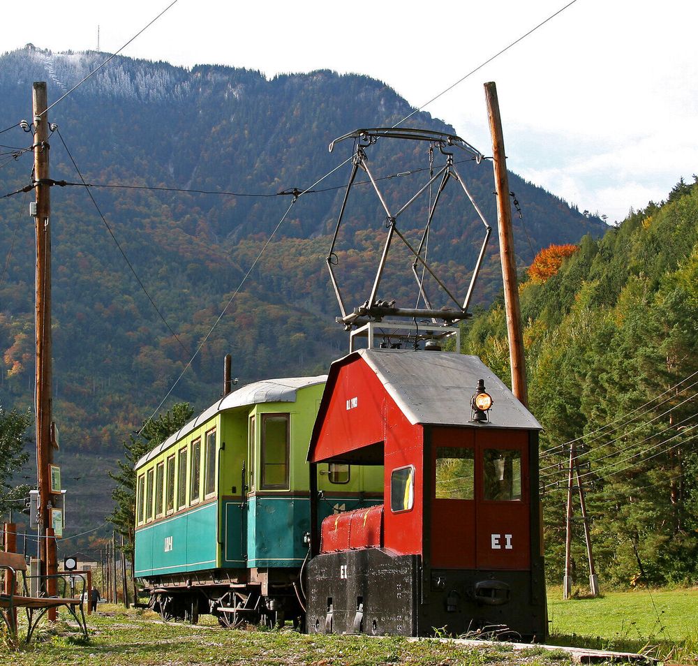 Historischer grün-gelber Triebwagen steht auf Gleisen mit Berge im HIntergrund.